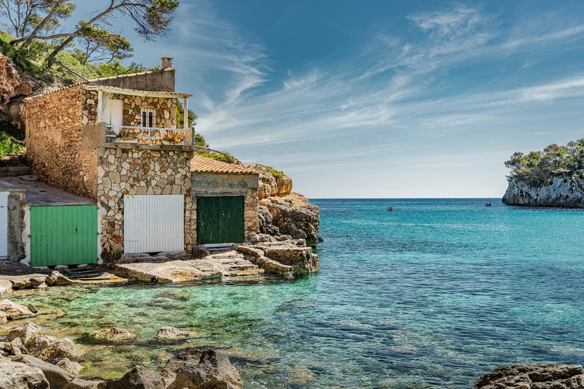 Mallorca'nın güneydoğu kıyısında turkuaz bir koya yakın geleneksel taş tekne barınakları, kayalık sahil, berrak su ve denize doğru uzanan manzarasıyla.