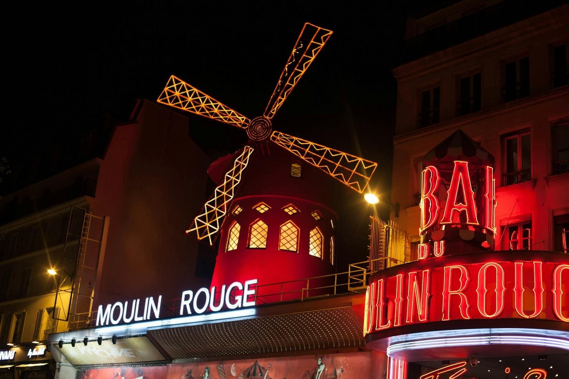 Vue nocturne du cabaret Moulin Rouge illuminé à Paris, avec le célèbre moulin rouge et ses enseignes au néon vibrantes sur la façade du bâtiment.