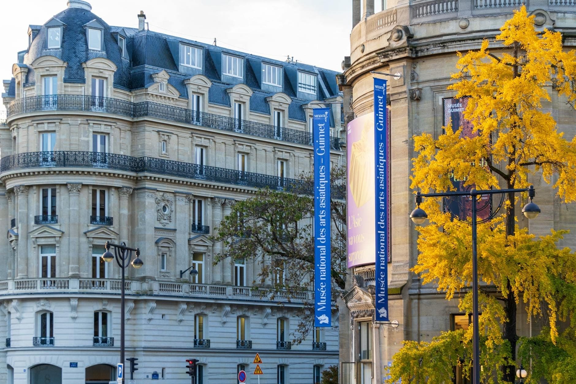 Elegant neoclassical building with blue banners reading 'Musée national des arts asiatiques – Guimet', surrounded by trees and city architecture on a sunny day.