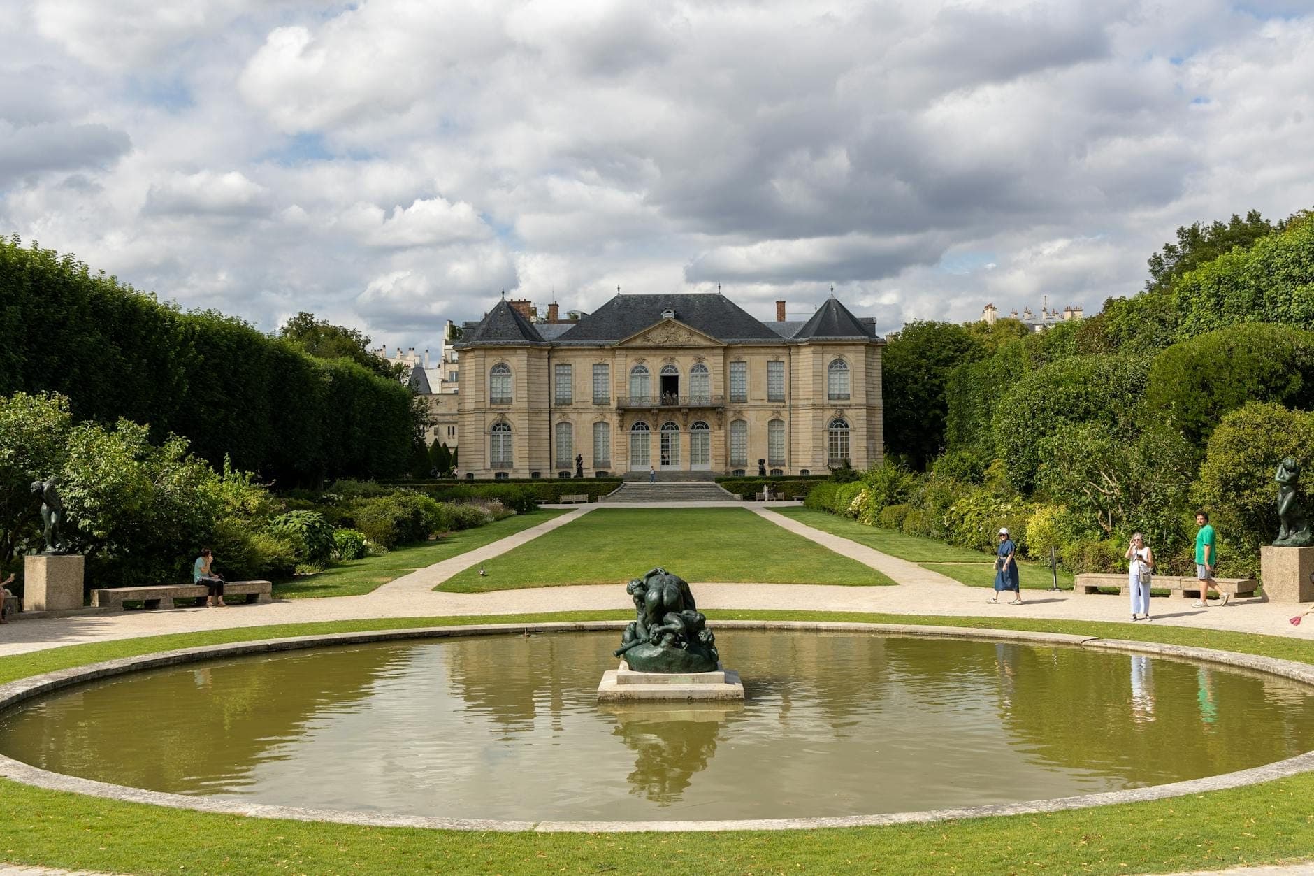 The Hôtel Biron at Musée Rodin with formal gardens, a pond, and Rodin’s The Thinker sculpture in the center foreground under a dramatic sky.