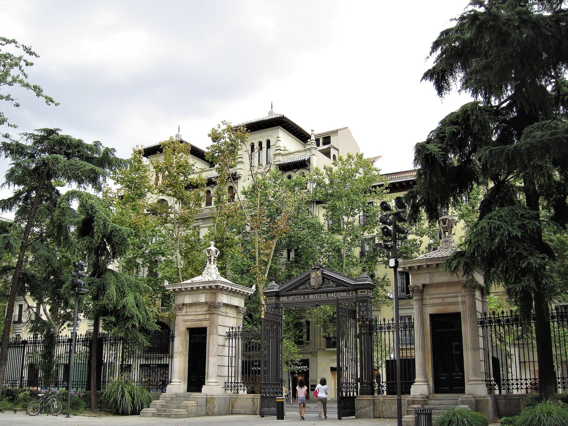 ประตูทางเข้าอันยิ่งใหญ่และด้านหน้าอาคารประวัติศาสตร์ของ Museo Arqueológico Nacional ในมาดริด ล้อมรอบด้วยต้นไม้เขียวขจีในวันที่มีเมฆมาก
