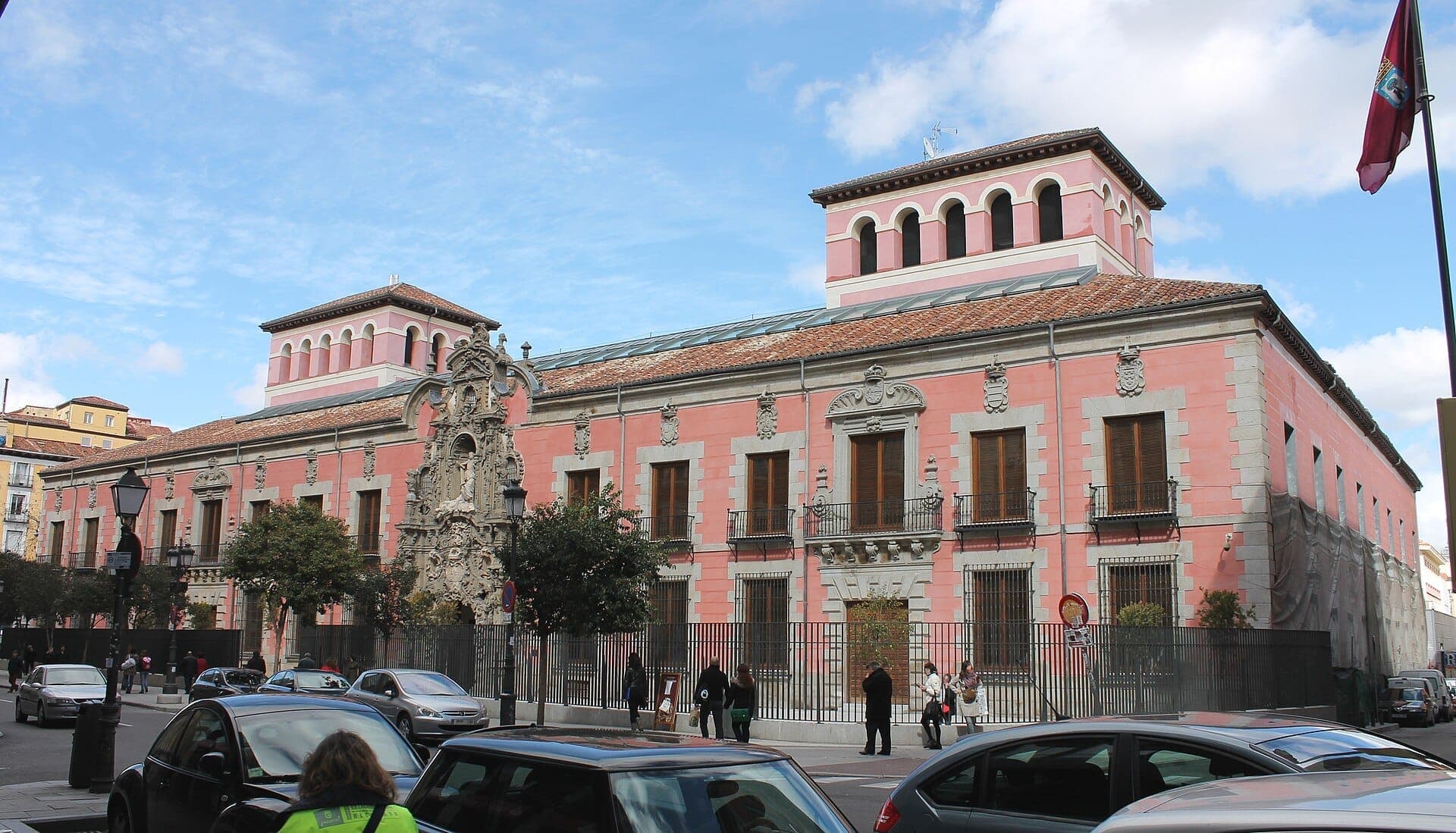 ด้านหน้าสไตล์บาโรกสีชมพูของ Museo de Historia de Madrid พร้อมงานหินประดับอันวิจิตร หน้าต่างสูง และผู้คนที่เดินผ่านในวันที่แดดจ้า