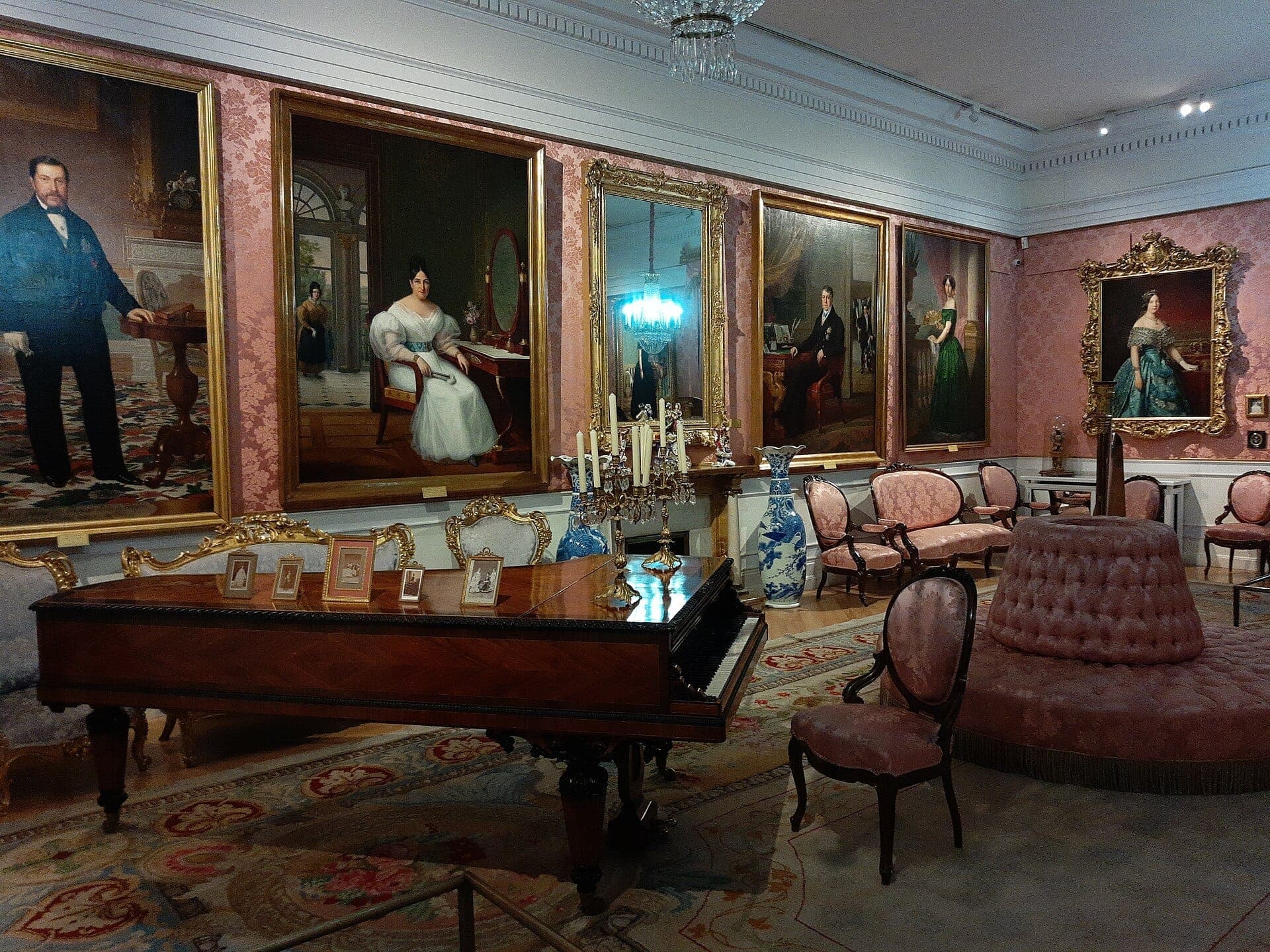 ห้องรับรองสไตล์หรูหราในศตวรรษที่ 19 ณ Museo del Romanticismo ตกแต่งด้วยเฟอร์นิเจอร์โบราณ เปียโนหางช้าง และภาพเหมือนกรอบทองบนผนังลายวอลเปเปอร์สีชมพู