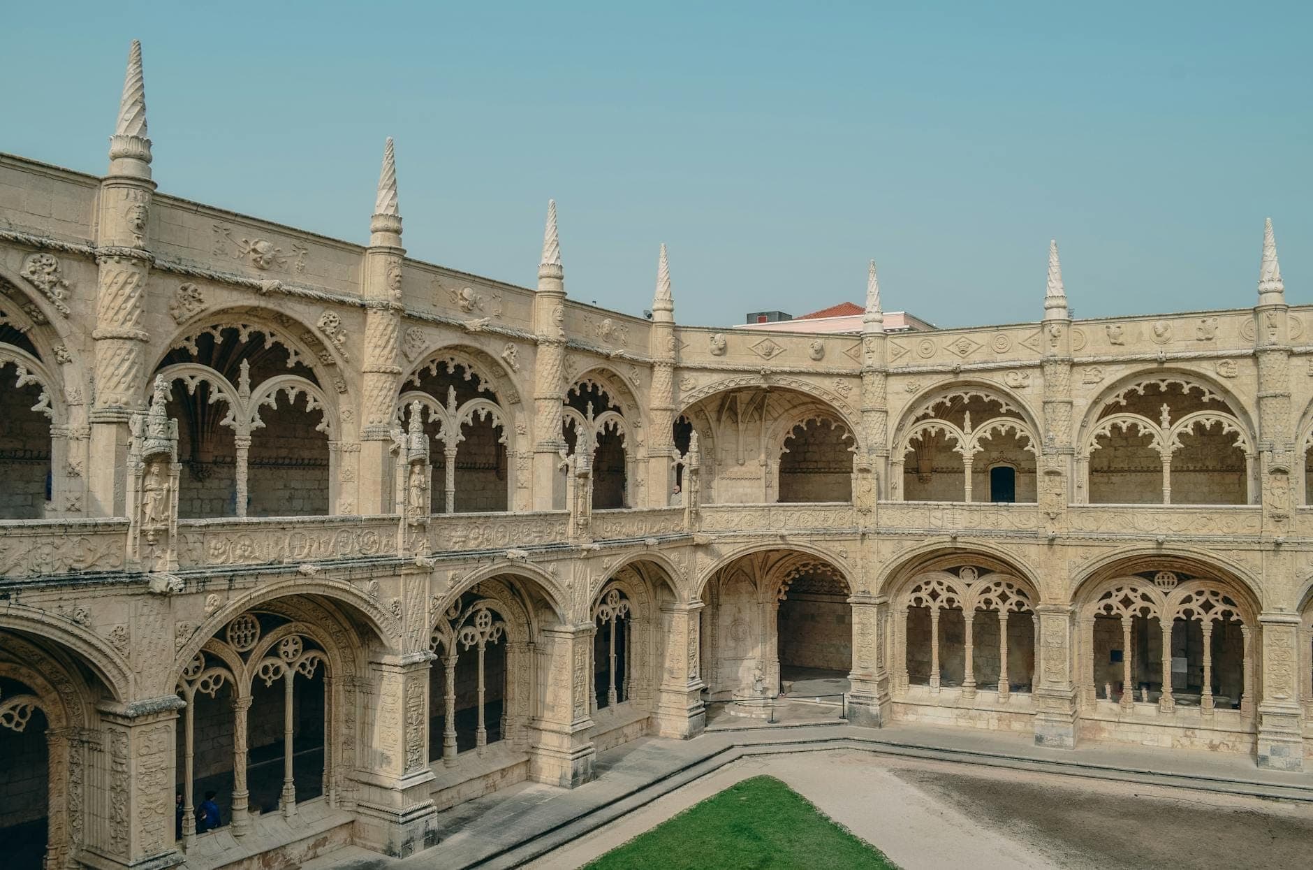 Vista deslumbrante dos claustros ornamentados em pedra do Mosteiro dos Jerónimos, com arcos e torres sob um céu límpido, exibindo a arquitetura histórica de Portugal.
