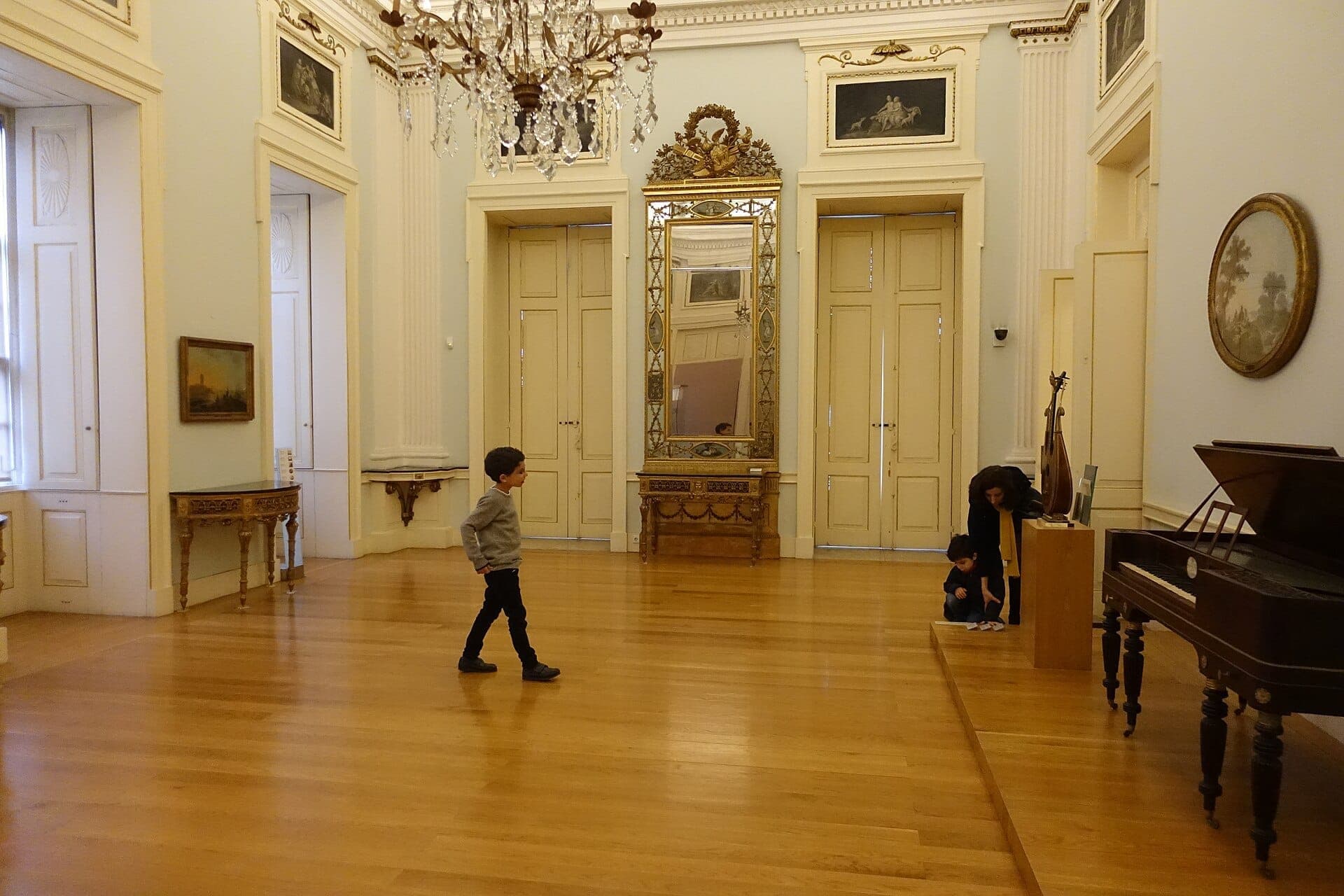 Elegante sala della galleria all'interno del Museu Nacional Soares dos Reis con pavimenti in parquet, lampadari, specchi ornati e visitatori che esplorano il tranquillo interno neoclassico.