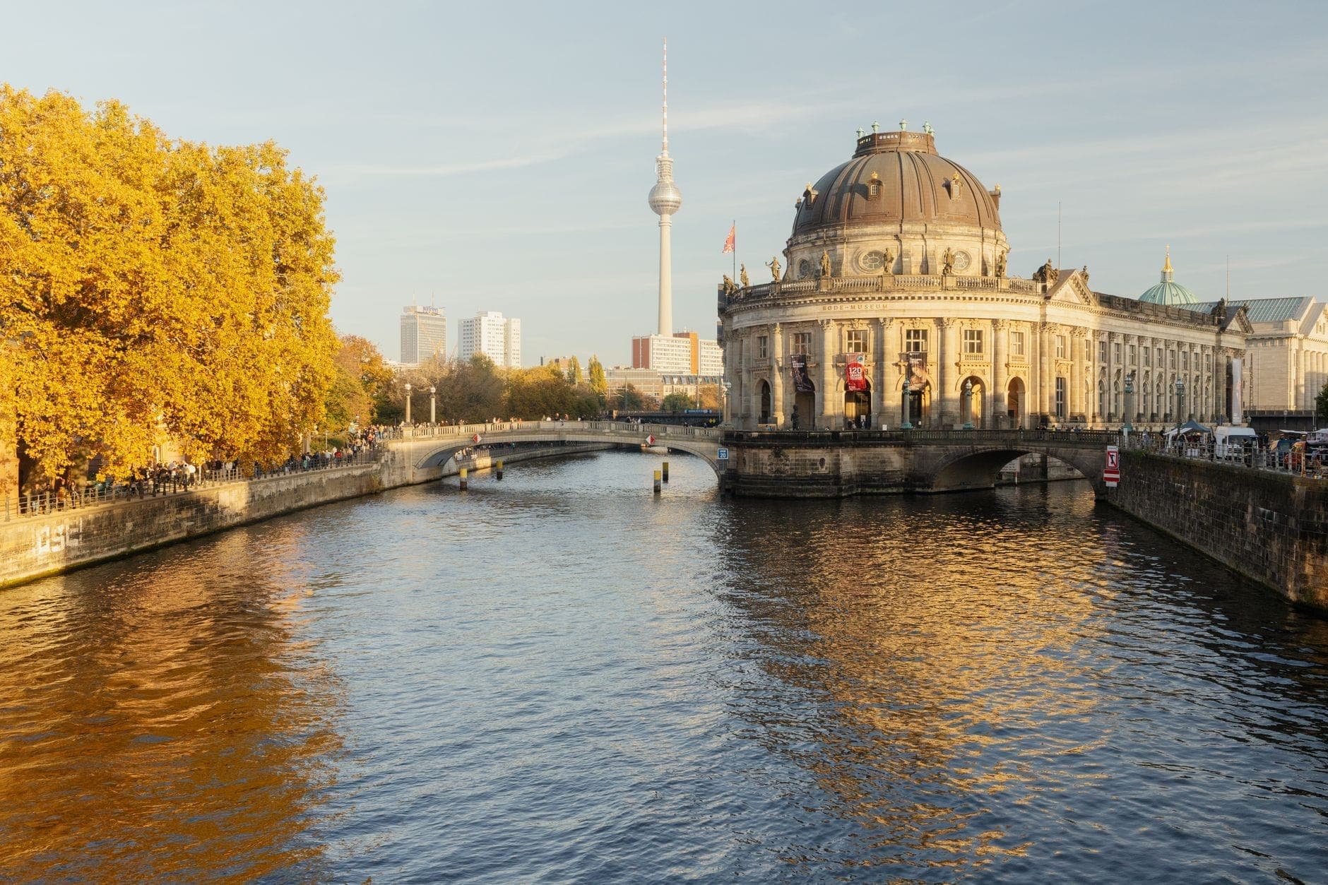 L'Isola dei Musei a Berlino con il Bode-Museum, la torre televisiva sullo sfondo e il fiume Spree in primo piano in una giornata di sole.