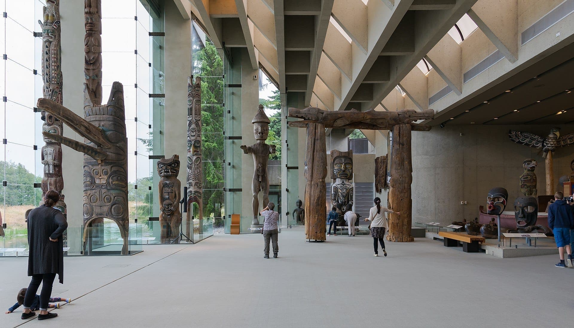 แกลเลอรีหลักของ Museum of Anthropology ที่ UBC ที่มีเสาโทเทมของชนพื้นเมืองสูงตระหง่าน งานแกะสลักไม้ กำแพงคอนกรีต และผู้เข้าชมที่กำลังสำรวจนิทรรศการ