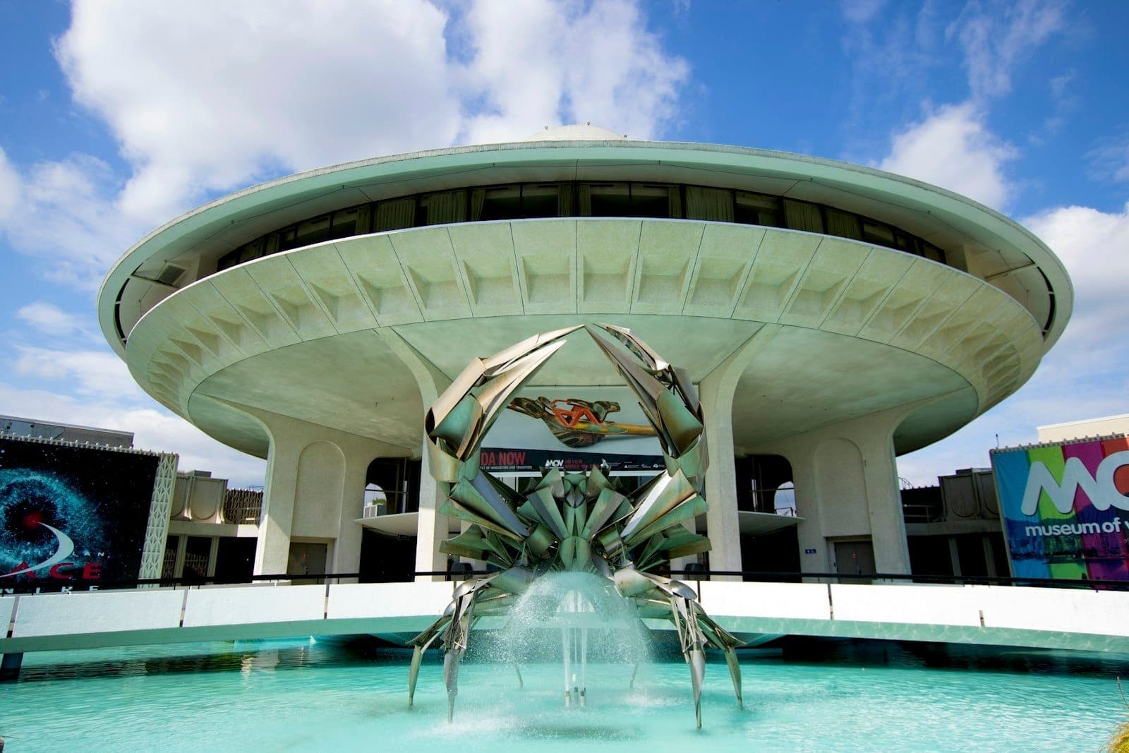 มุมมองด้านหน้าของ Museum of Vancouver โดดเด่นด้วยอาคารทรงจานบินอันเป็นเอกลักษณ์ ประติมากรรมปูสแตนเลส และท้องฟ้าสีฟ้าสดใส