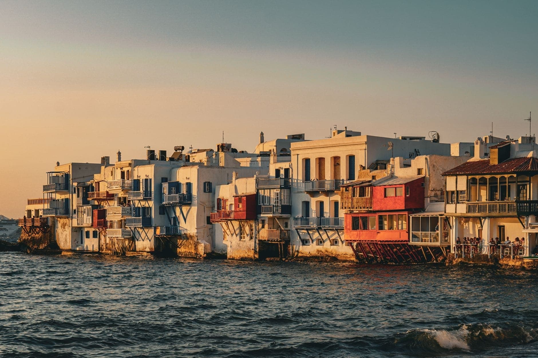 Klein Venedig in Mykonos bei Sonnenuntergang, mit den ikonischen Bars an der Uferpromenade und weiß getünchten Gebäuden am Meer.