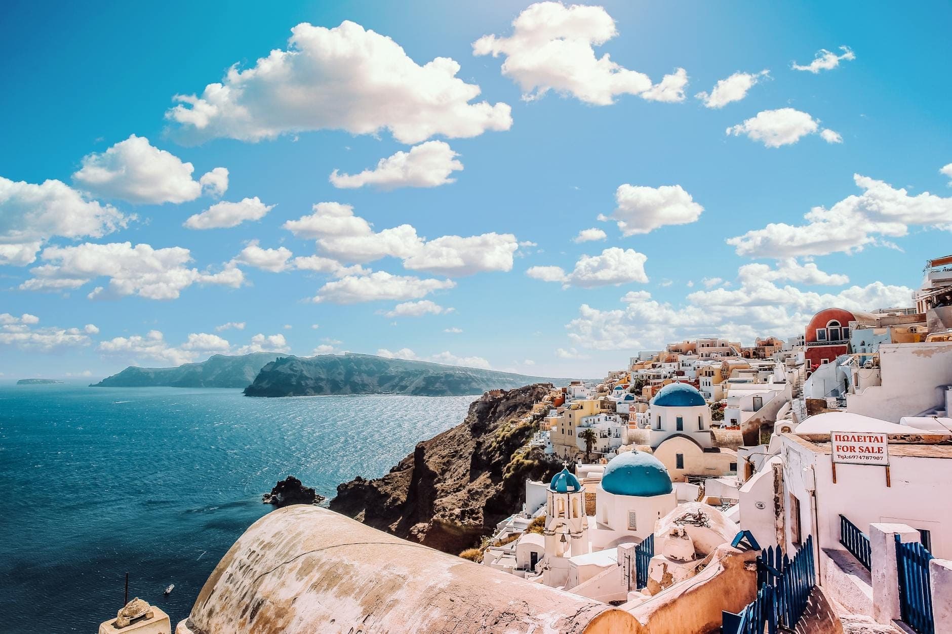 Atemberaubendes Panorama von Santorini mit den ikonischen blau gewölbten Kirchen, weißen Häusern und dramatischen Klippen mit Blick auf das glitzernde Ägäische Meer an einem sonnigen Tag.