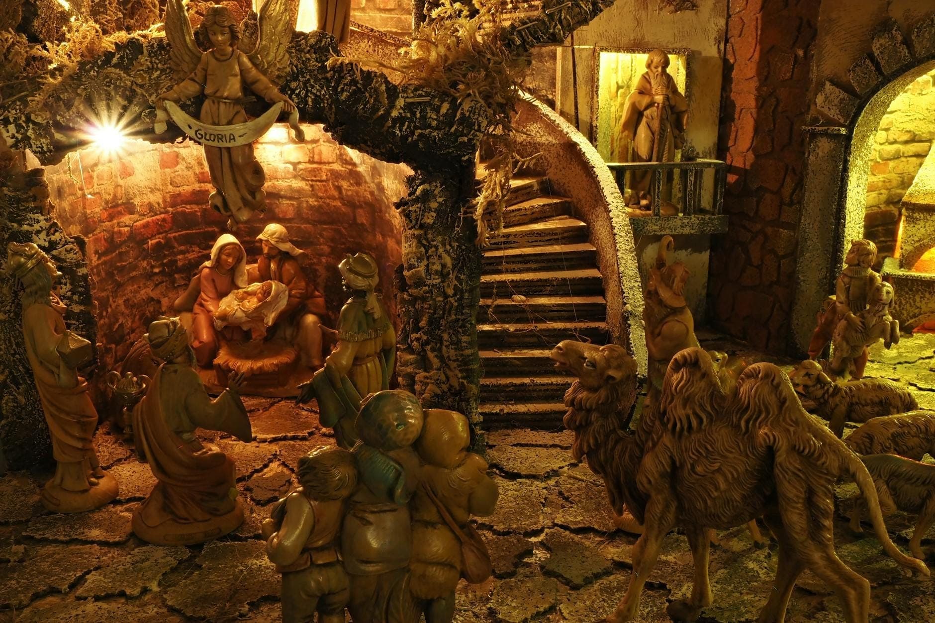 Presépio elaborado com muitas figuras detalhadas, animais e arquitetura de aldeia sob uma iluminação calorosa, lembrando um tradicional presepe napolitano.