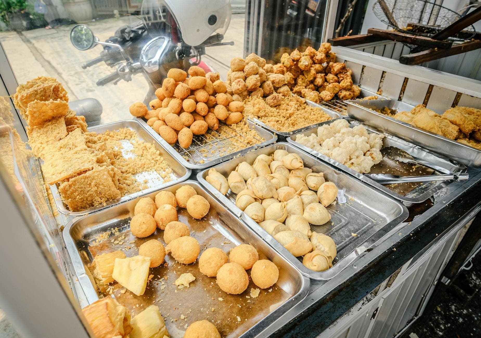Close-up de uma barraca de comida de rua em Nápoles exibindo bandejas com salgadinhos fritos variados como arancini e crocche em uma calçada movimentada.