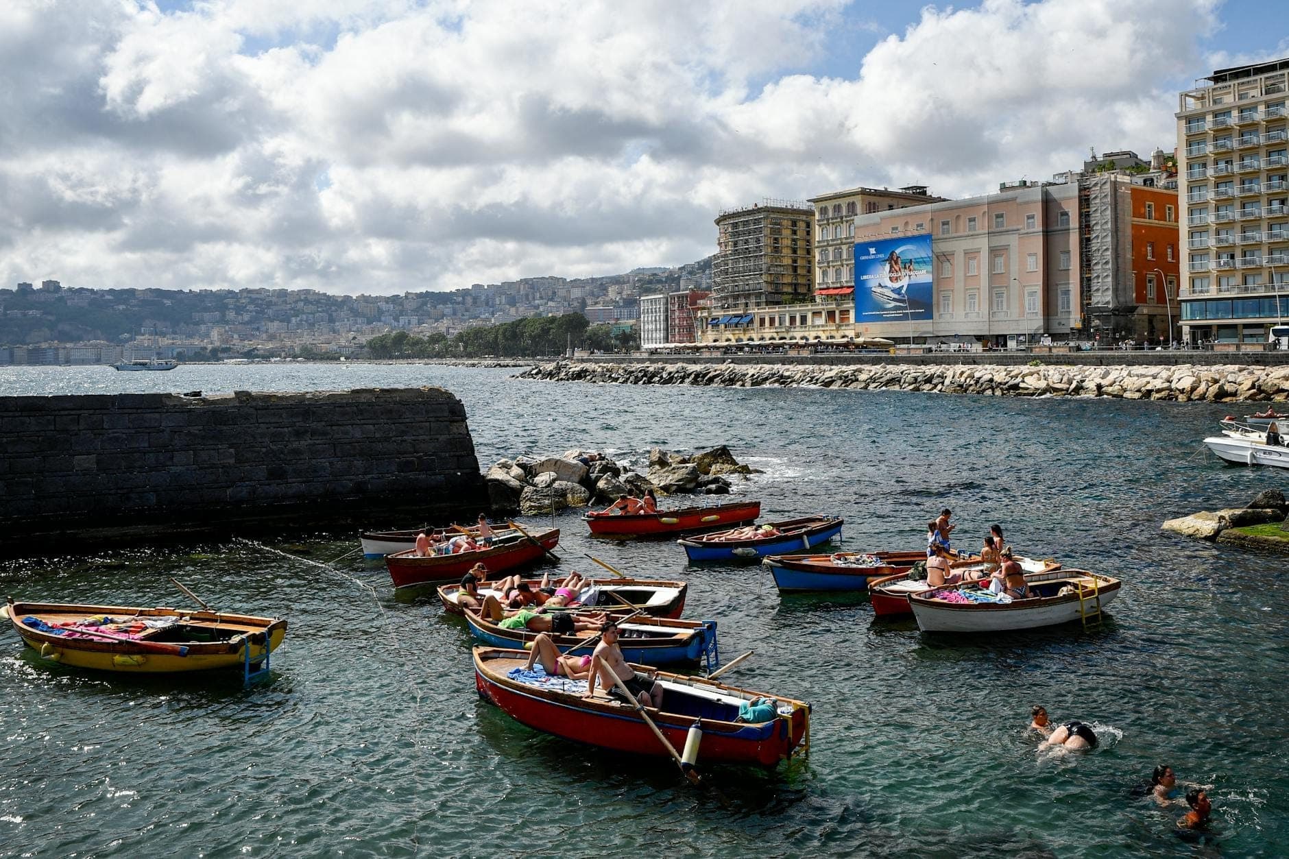 Barcos coloridos na orla marítima de Nápoles com elegantes hotéis e edifícios ao longo da avenida à beira-mar.
