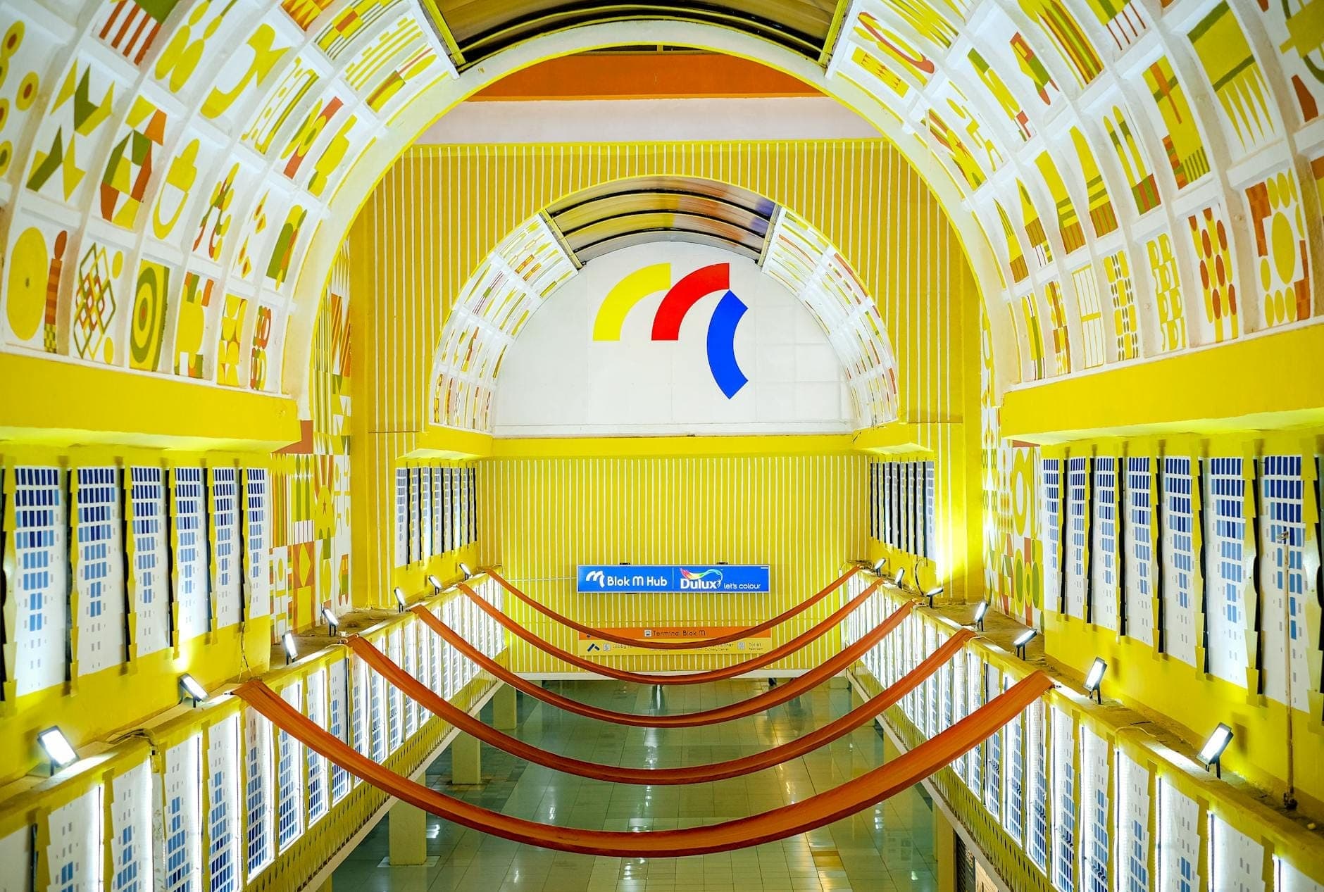 Estação de metrô de Nápoles bem iluminada com decoração amarela, arcos artísticos e uma placa azul da estação com o nome 'Dante' acima da plataforma.