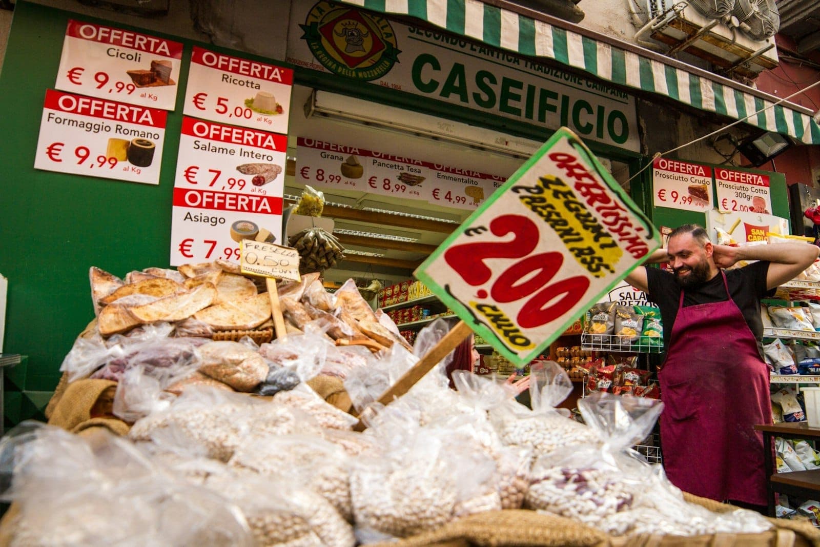 Uma movimentada barraca de street food em Nápoles com cestos de salgadinhos fritos tradicionais, placas escritas à mão e um vendedor à frente, capturando a cultura local de comida de rua.