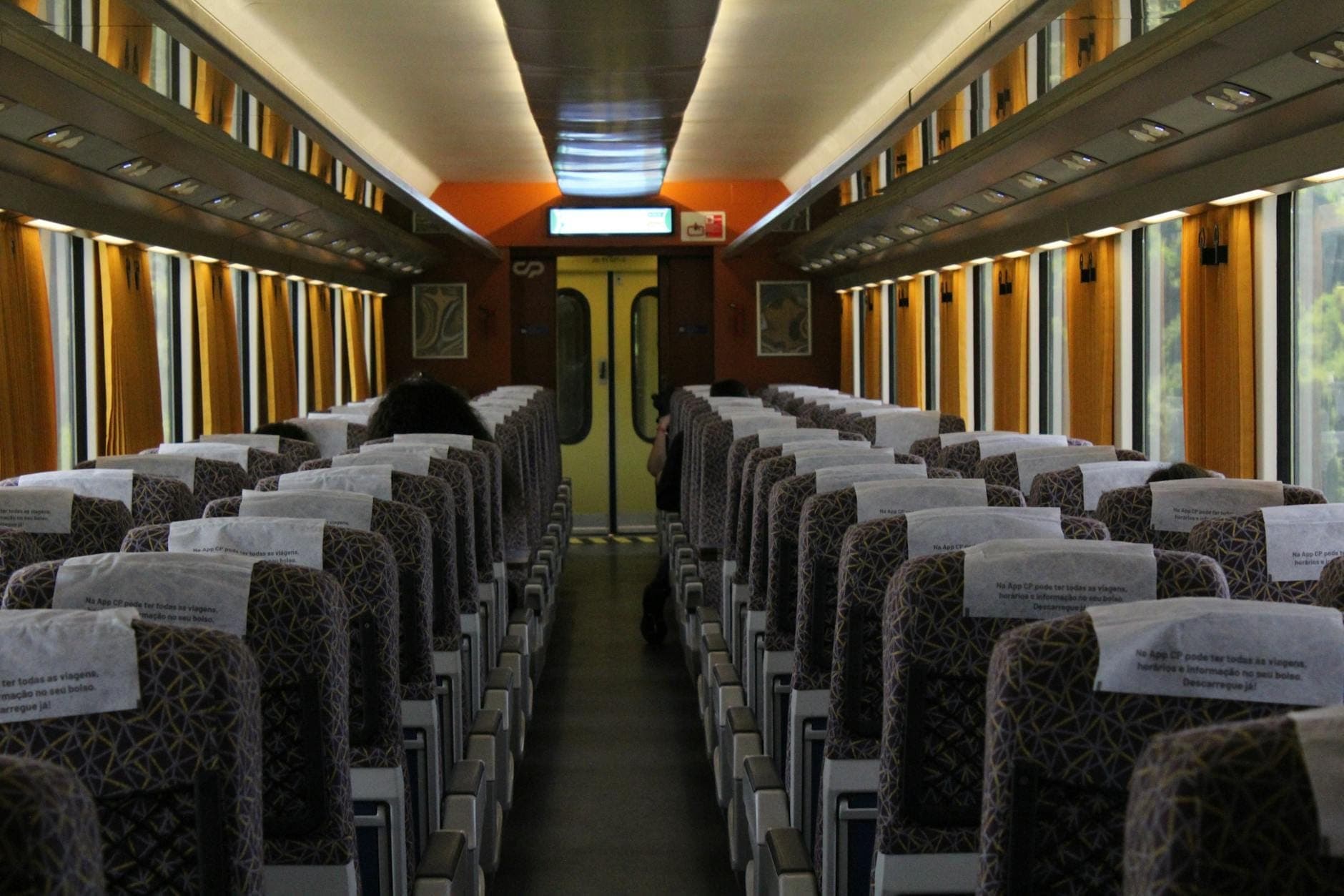 Interior iluminado de uma carruagem de comboio com fileiras de assentos estampados e detalhes em laranja, sugerindo uma viagem de trem regional italiano.