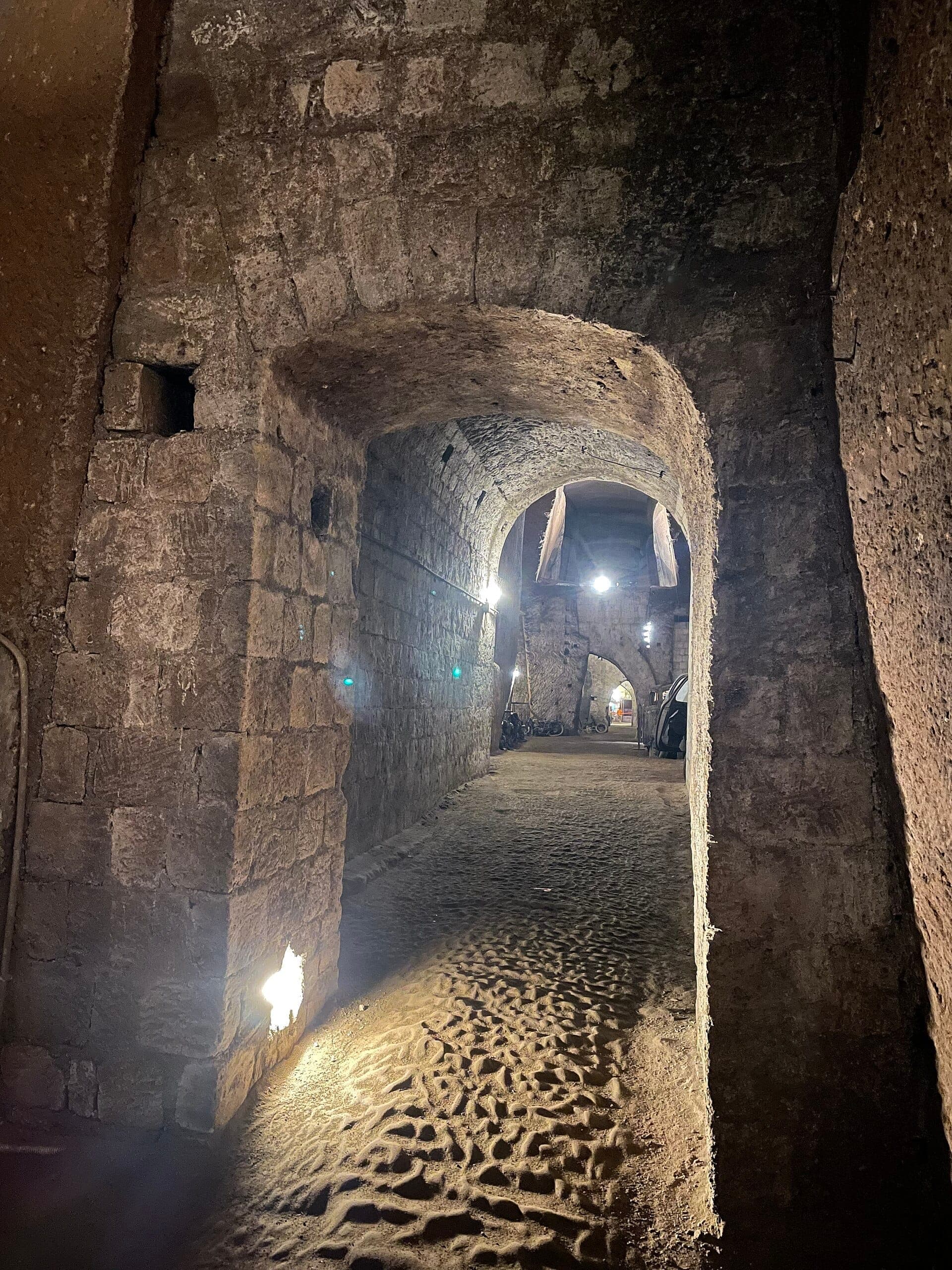 Arcos de pedra e paredes ásperas dos túneis de Napoli Sotterranea, iluminados por uma luz suave, mostrando a antiga arquitetura subterrânea sob Nápoles.