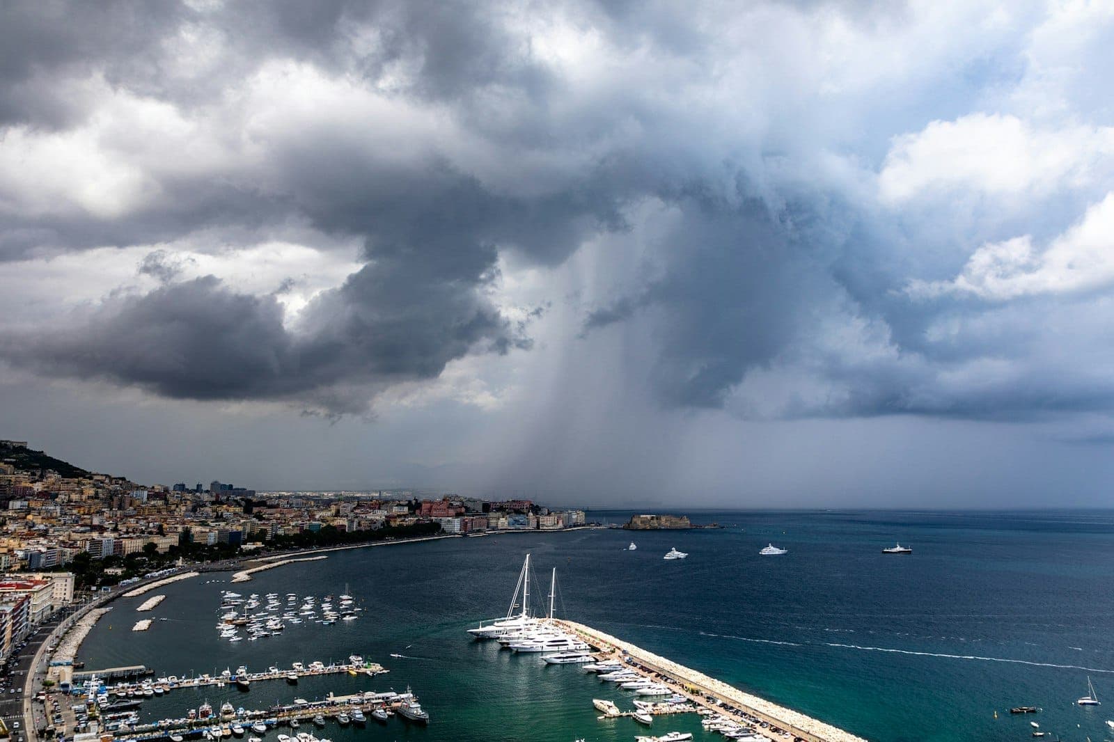 Vista panorâmica de Nápoles, Itália, com o calçadão, a marina com barcos e dramáticas nuvens de tempestade sobre a cidade.