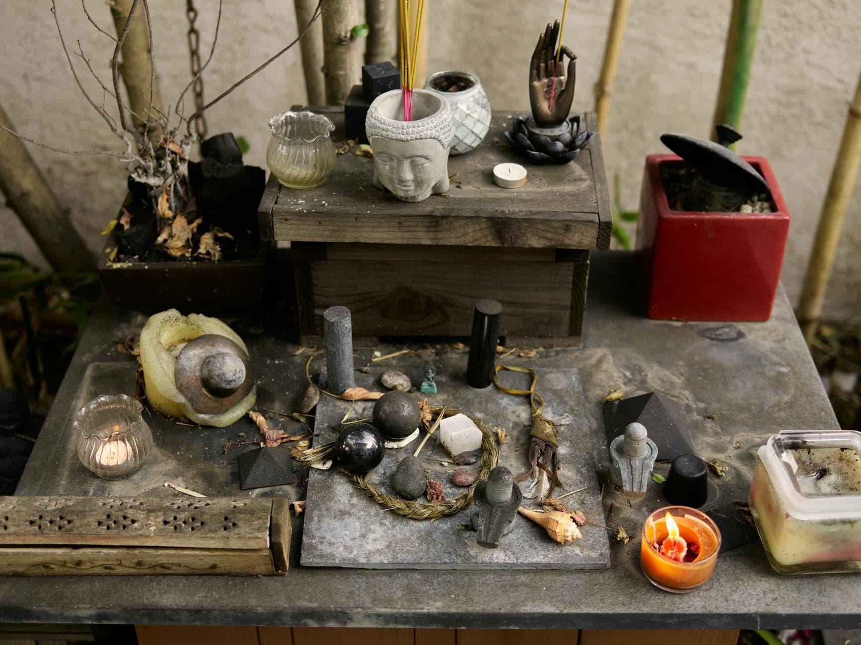 Altar ou santuário ao ar livre coberto de velas, figurinhas, pedras, objetos esculpidos e incenso, evocando práticas religiosas populares.