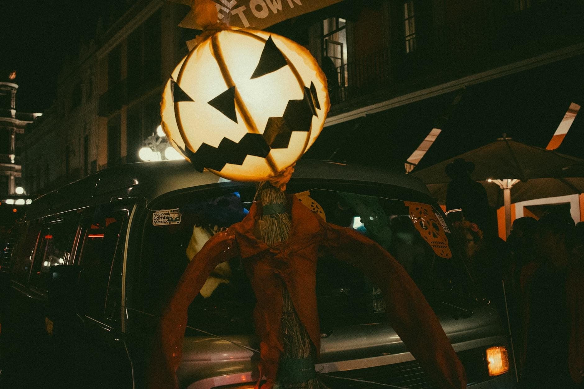 Large glowing jack-o-lantern decoration with a wide grin set against a lively nighttime street scene, capturing festive Halloween energy in New Orleans.