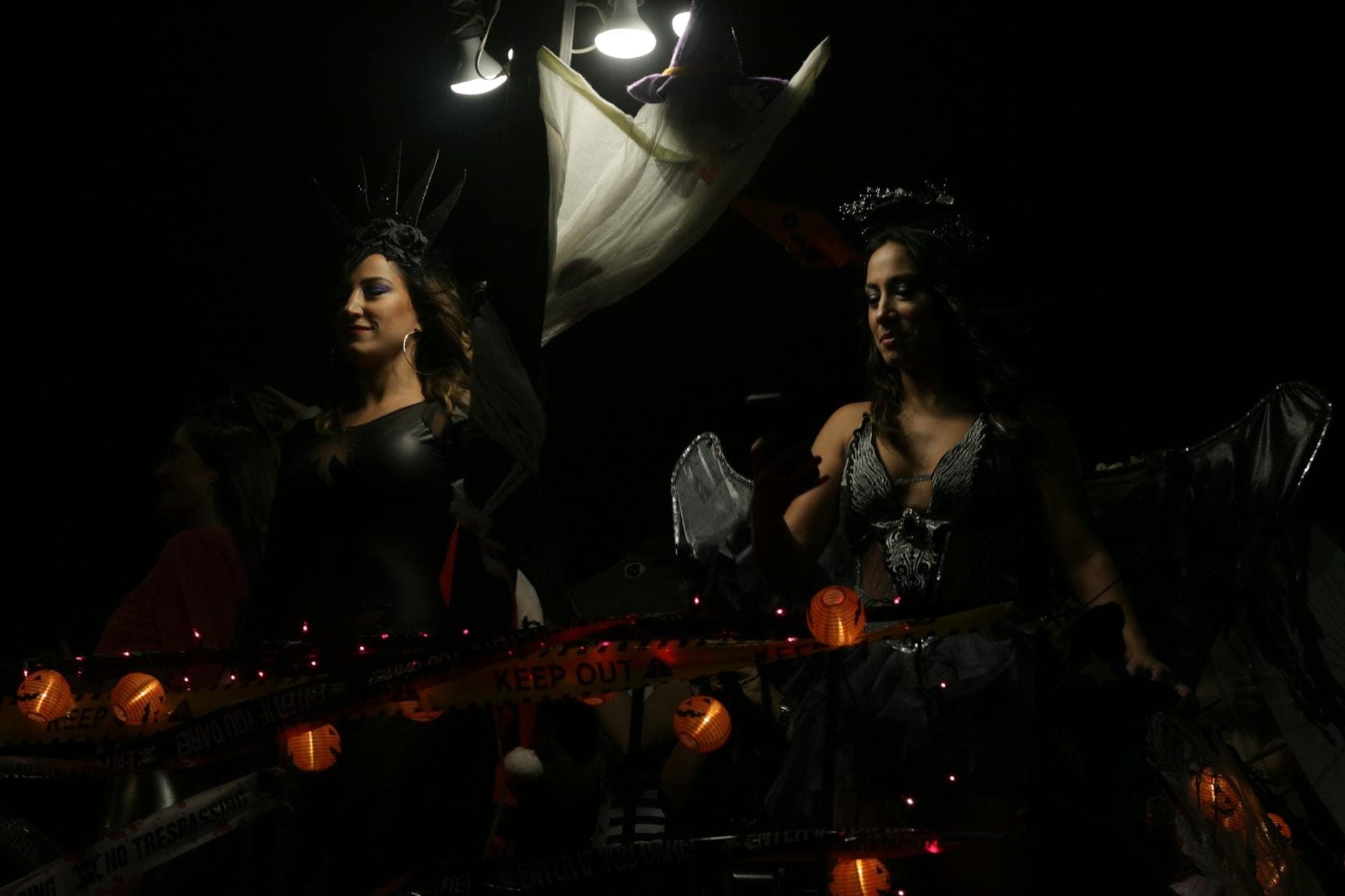 Due donne in elaborati costumi neri su un carro decorato con luci di Halloween e nastro di segnalazione di notte.