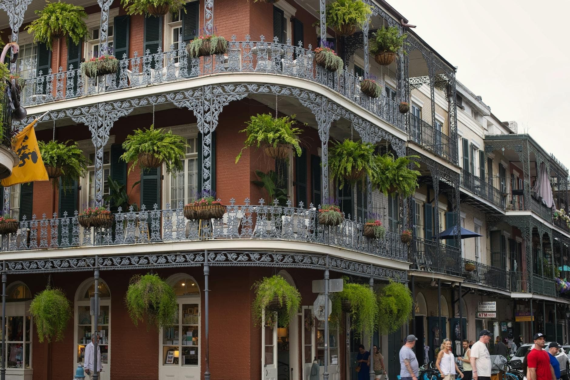 Historyczny budynek French Quarter w New Orleans z ozdobnymi balkonami z kutego żelaza i wiszącymi roślinami, z tłumem ludzi na chodniku.
