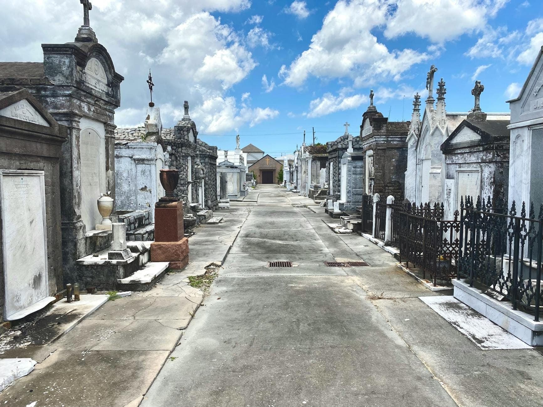 Naziemne grobowce i mauzolea na historycznym cmentarzu w New Orleans pod jasnym błękitnym niebem z chmurami.