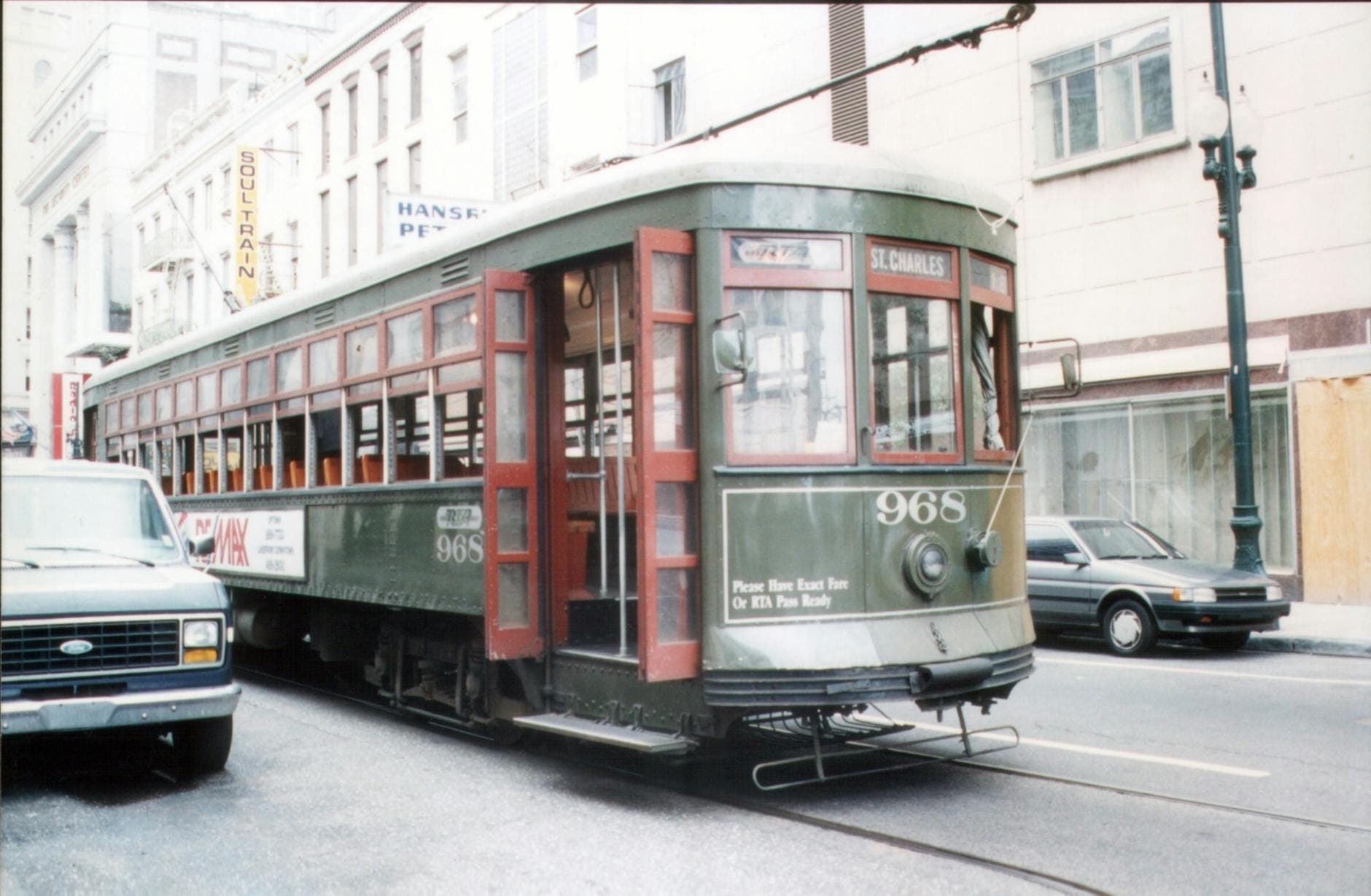 Klasyczny zielony tramwaj z oznaczeniem St. Charles na ulicy New Orleans z samochodami i budynkami w tle.