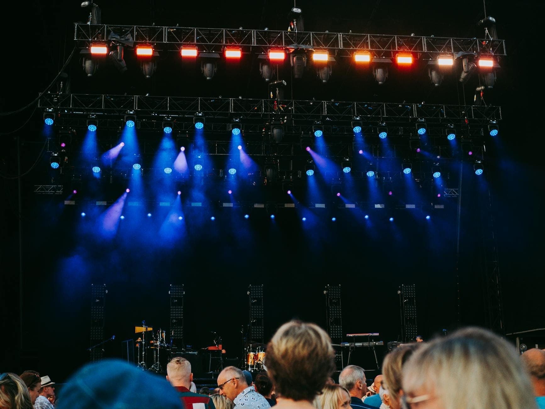Bühne eines Open-Air-Musikfestivals mit bunten Lichtern und einem sich davor versammelnden Publikum, bereit für eine Live-Aufführung.