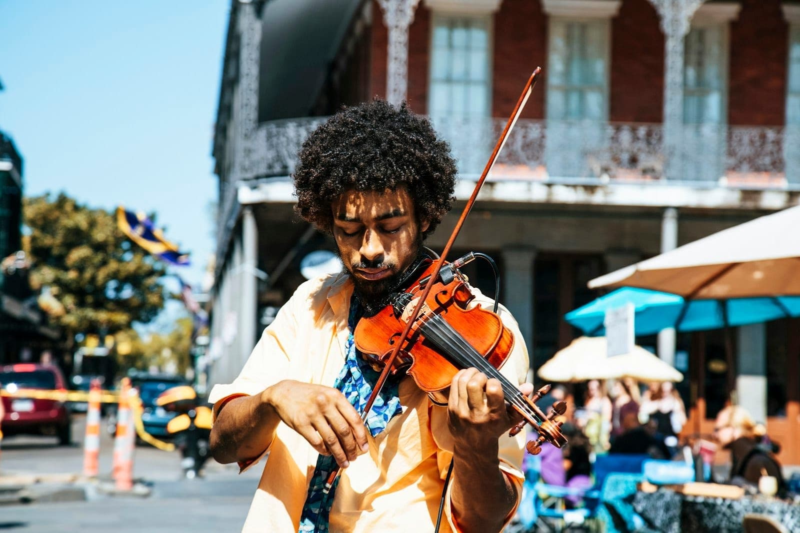 Street musician playing violin in the French Quarter of New Orleans, with iron balconies and colorful umbrellas on a sunny day.