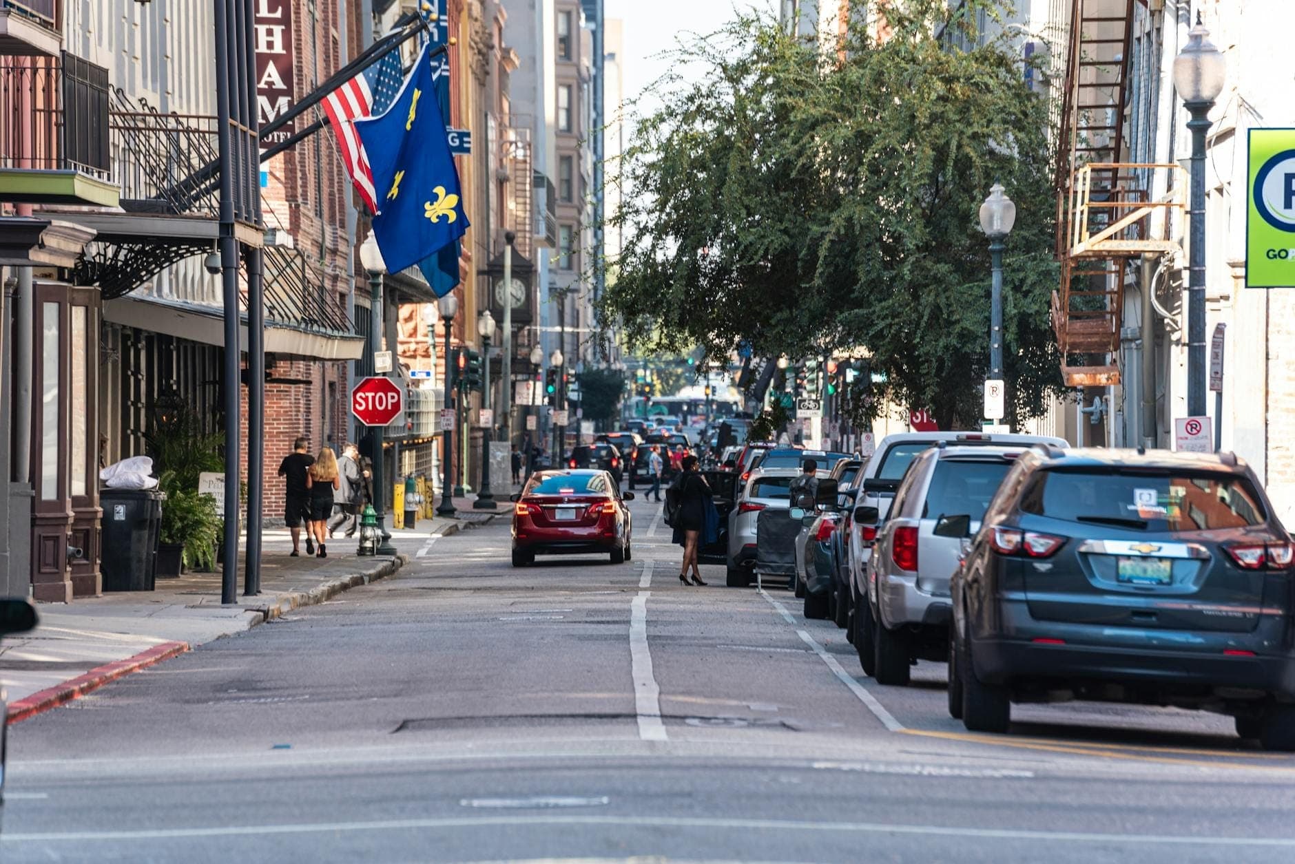 Uma movimentada rua do centro de New Orleans com carros estacionados, pedestres e bandeiras, mostrando um ambiente urbano animado.