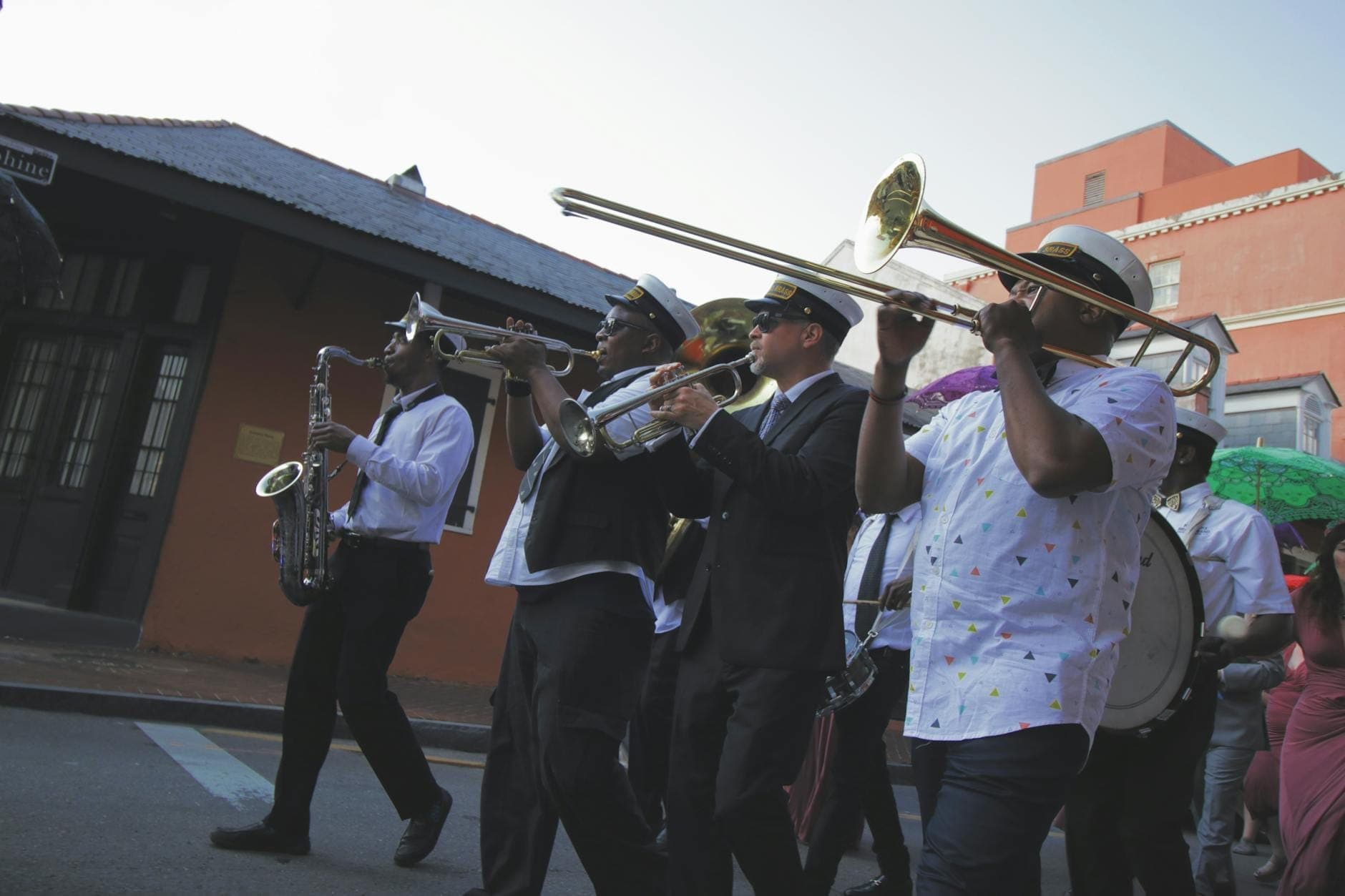 Brass band musicians in uniform and hats parade down a street, playing instruments during daylight in New Orleans.