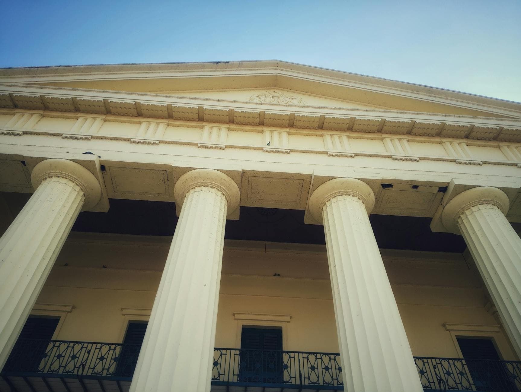 Aufnahme aus niedrigem Winkel eines historischen Greek Revival-Gebäudes mit großen Säulen und einem Balkon aus Schmiedeeisen unter blauem Himmel.