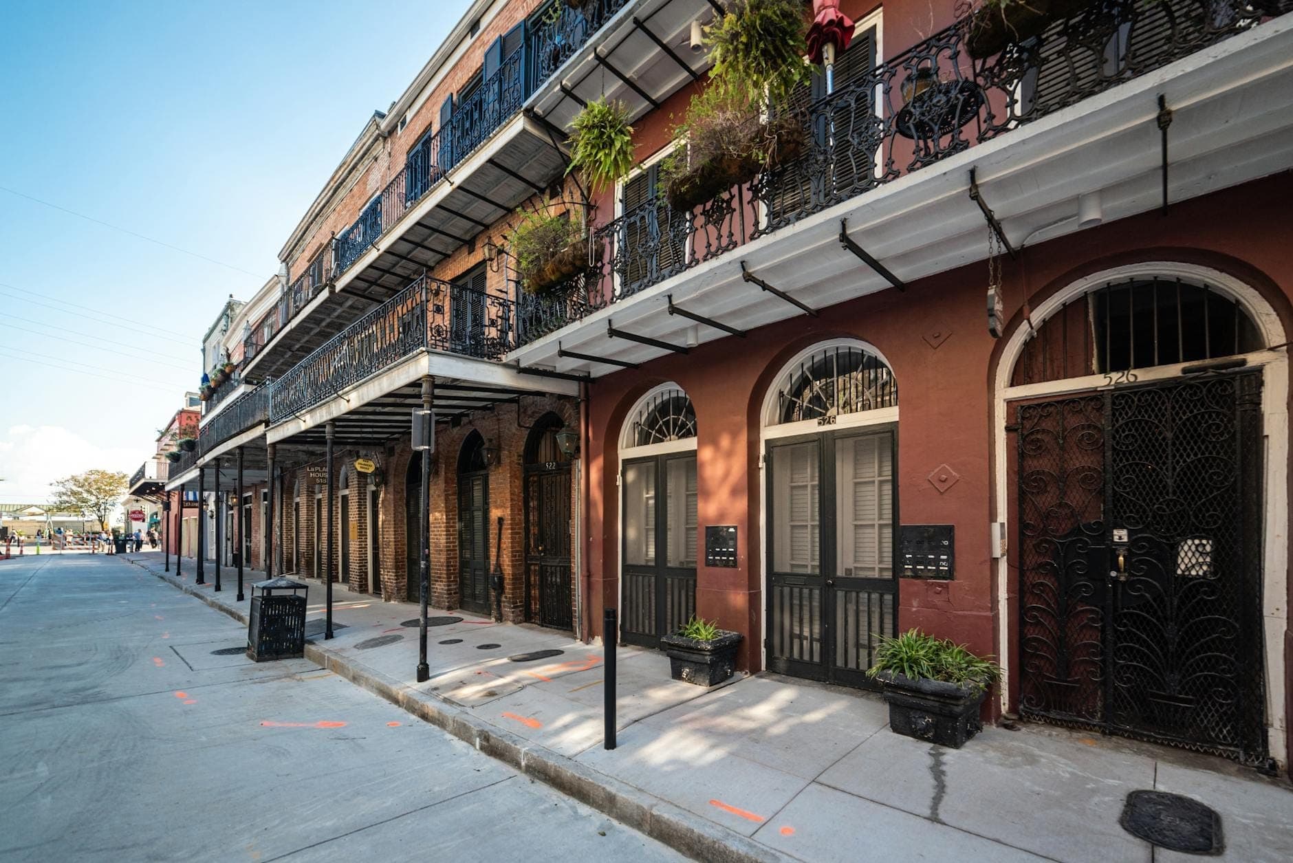 Straßenszene in New Orleans mit historischen Gebäuden, schmiedeeisernen Balkonen und Pflanzen, mit einem ruhigen Gehweg und blauem Himmel.