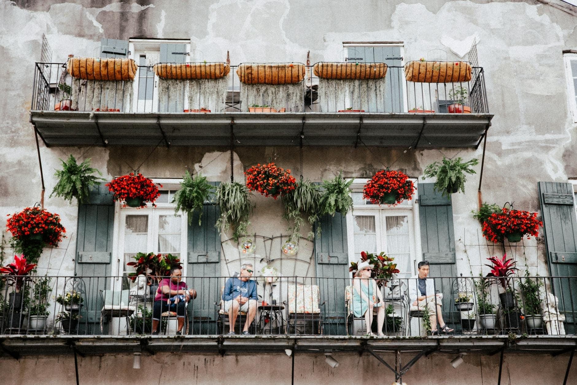 Families and children sit together on a classic New Orleans French Quarter balcony decorated with colorful flowers and plants, evoking a welcoming and lively family-friendly atmosphere.