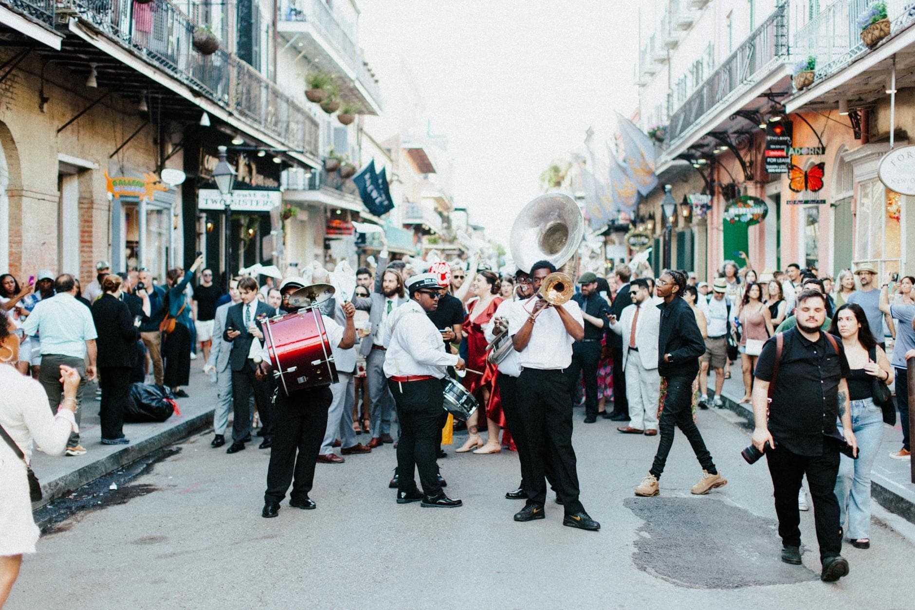 Một cảnh phố sôi động ở New Orleans với các nhạc sĩ chơi nhạc cụ đồng và mọi người tận hưởng bầu không khí lễ hội giữa những công trình kiến trúc đặc trưng của French Quarter.