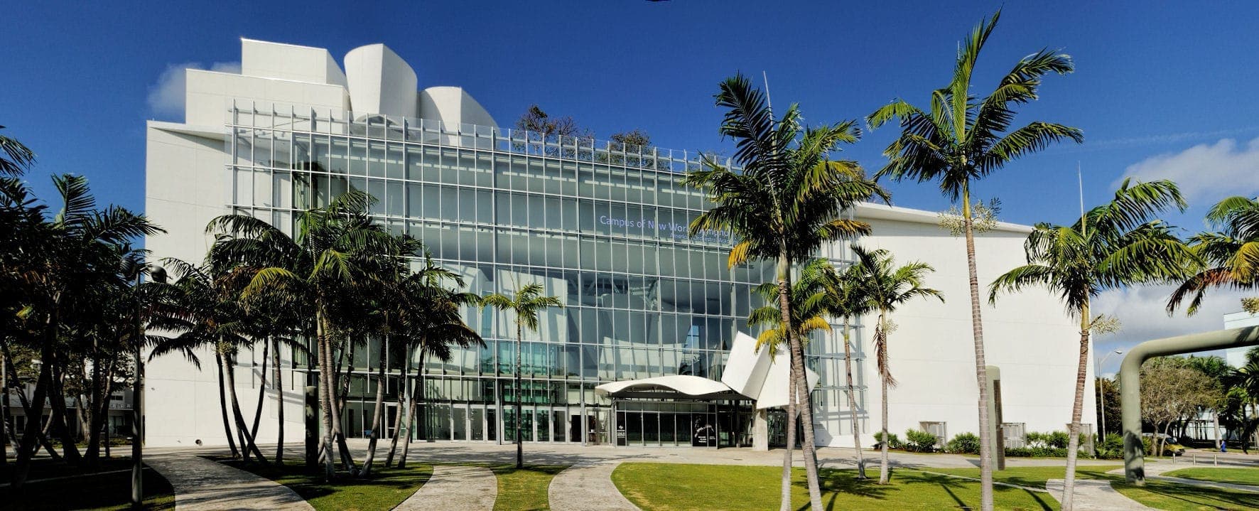 Modern glass facade of the New World Center concert hall, surrounded by palm trees and blue skies in Miami Beach, Florida.