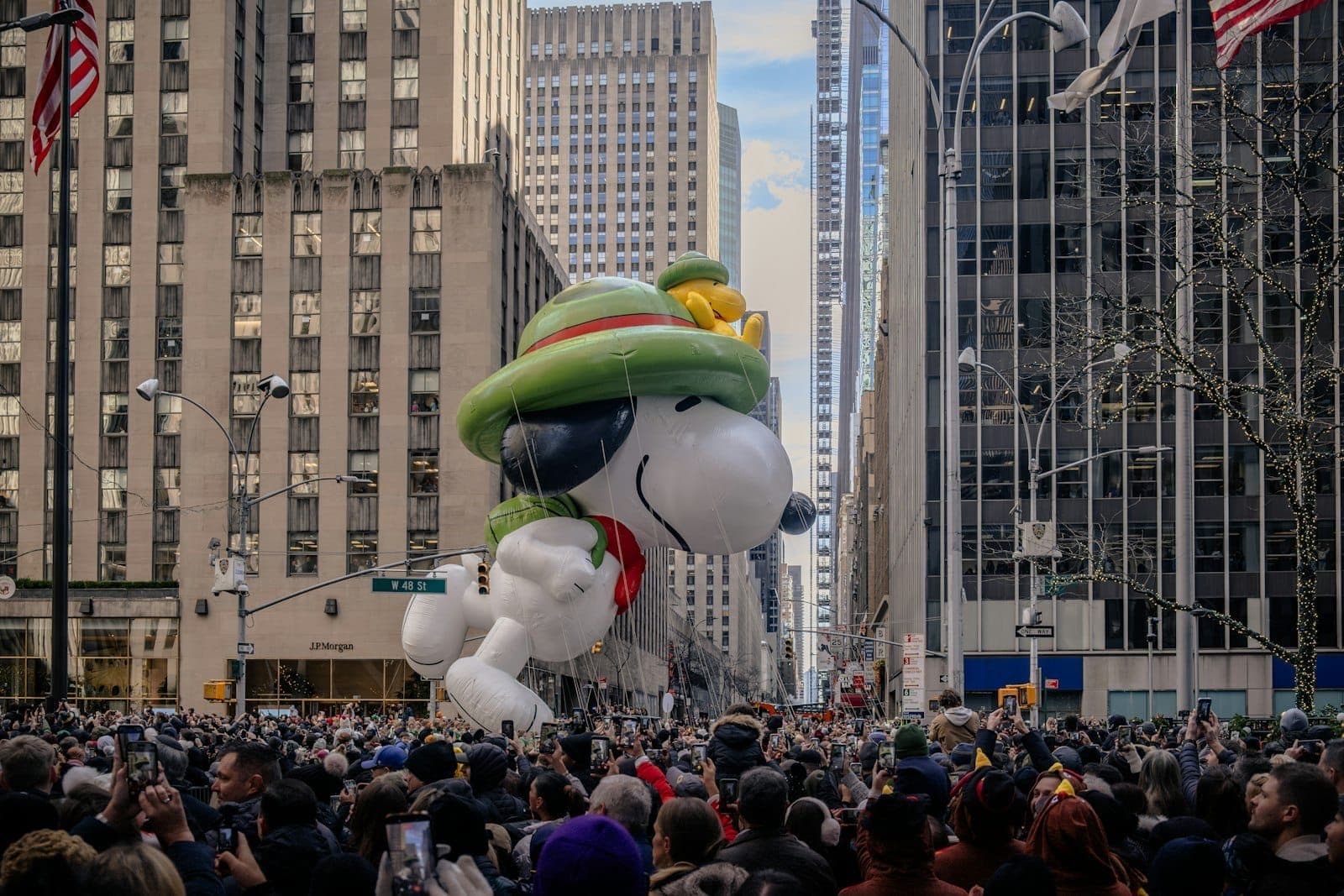 ฝูงชนจำนวนมากเรียงรายริมถนนในนิวยอร์กขณะลูกโป่งยักษ์ Snoopy ลอยผ่านตึกสูงในขบวนพาเหรดวันขอบคุณพระเจ้า Macy's