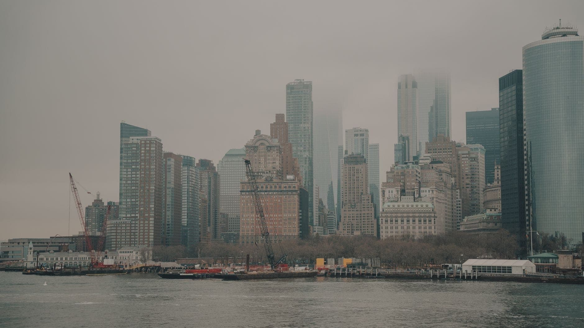 วิวท้องฟ้าครึ้มของเส้นขอบฟ้า Lower Manhattan จากฝั่งตรงข้ามแม่น้ำ โดยมีตึกระฟ้าสูงที่ถูกหมอกและเมฆบดบังบางส่วน