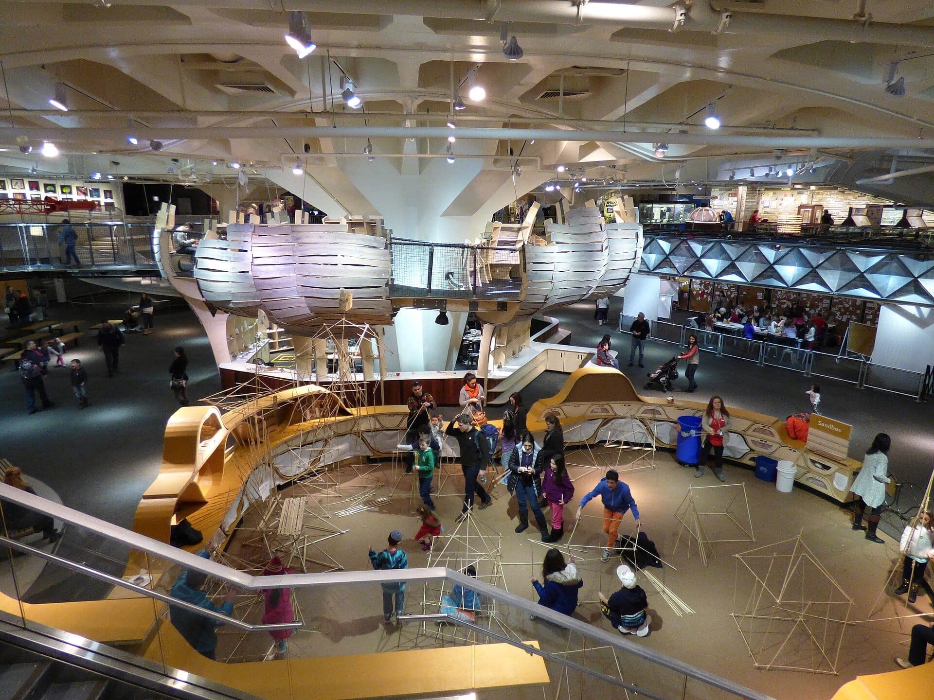มุมมองภายในของ New York Hall of Science ที่มีนิทรรศการเชิงโต้ตอบ โครงสร้างไม้ และผู้เยี่ยมชมที่สำรวจห้องโถงสมัยใหม่อันกว้างขวาง