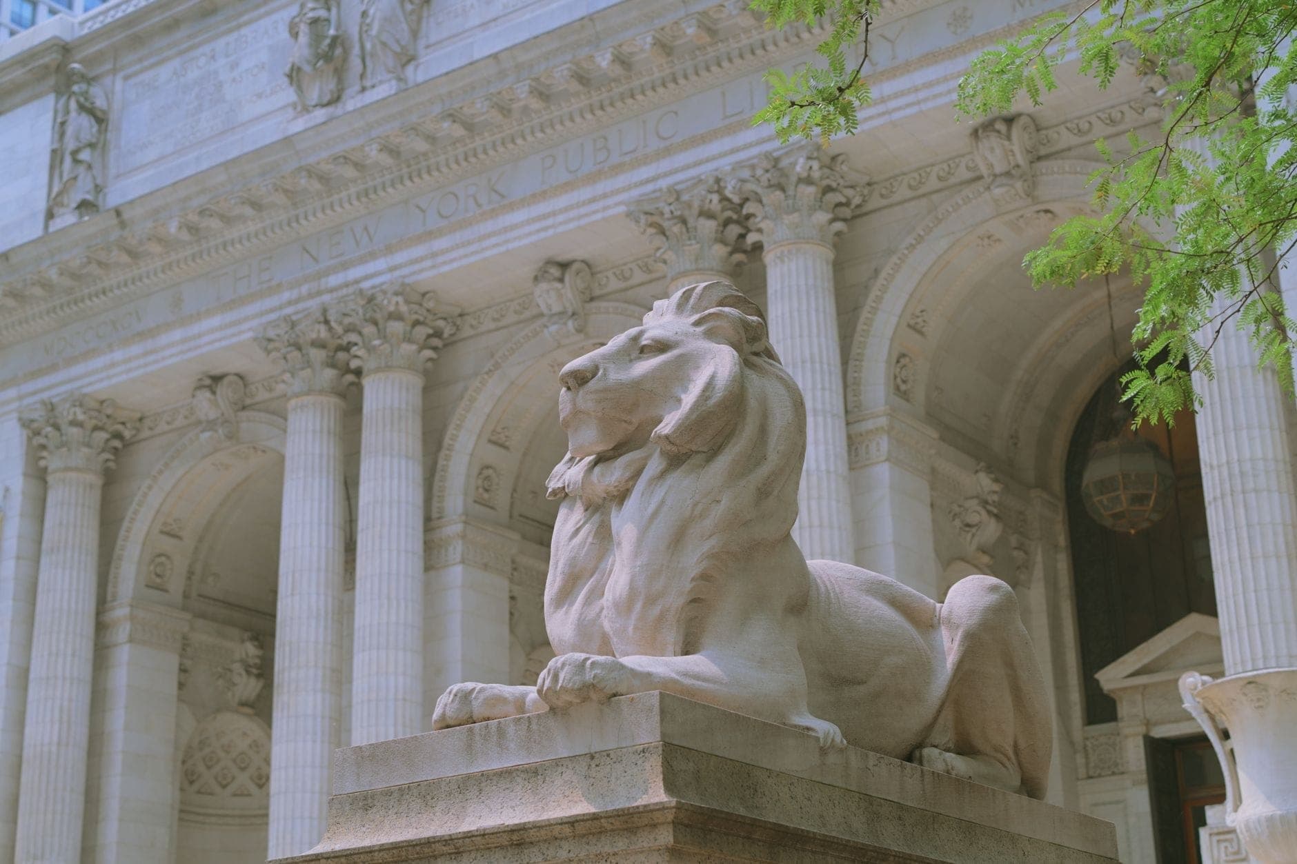 รูปปั้นสิงโตหินอ่อนอันโด่งดังหน้าทางเข้าอาคาร Stephen A. Schwarzman ของหอสมุดประชาชนนิวยอร์ก โดยมีเสาสูงและซุ้มประตูสไตล์บูซ-อาร์ตเป็นฉากหลัง
