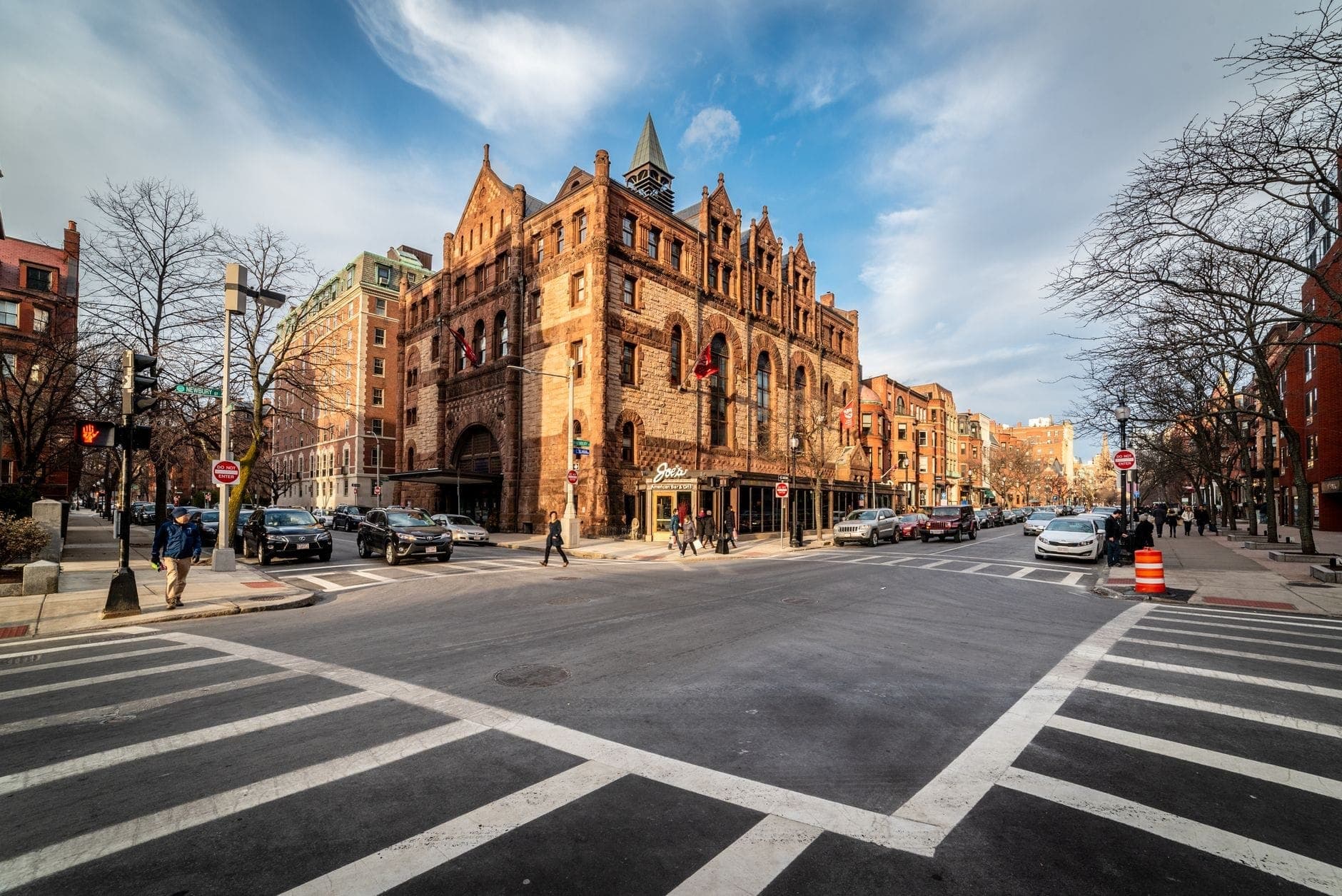 Vue large de Newbury Street dans le Back Bay de Boston avec son architecture victorienne en brique, ses passages piétons animés, ses promeneurs et un beau ciel, qui capture l'atmosphère vivante de la rue.