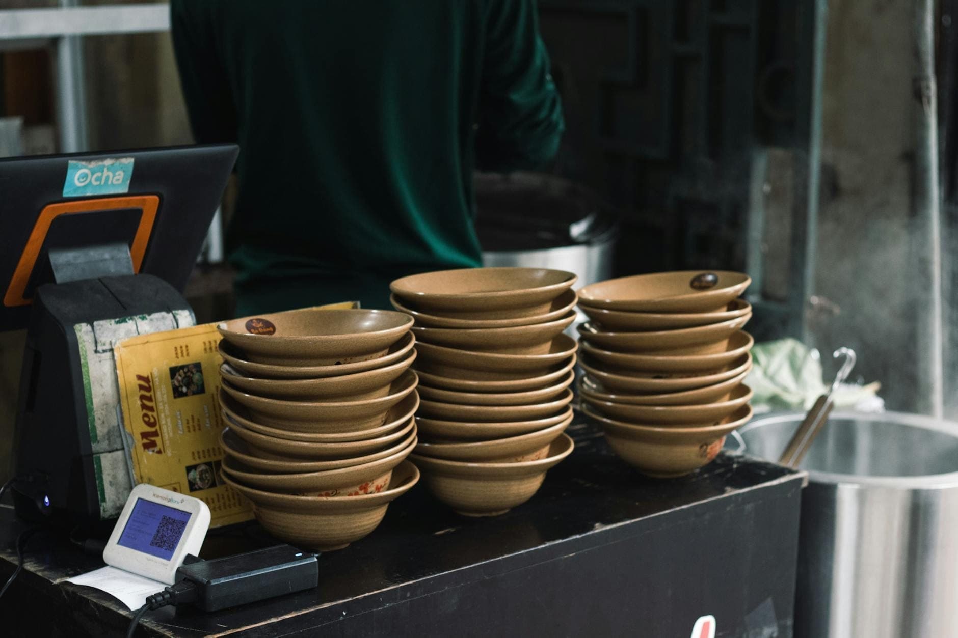 Стопка керамических мисок на стойке в обычном ресторане с видимыми меню и кассовым аппаратом.