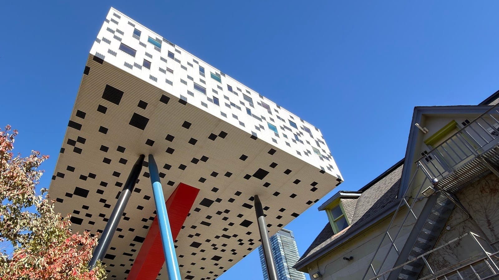 Il Sharp Centre for Design della OCAD University con la sua scatola pixelata in bianco e nero sollevata su colorate colonne inclinate contro un cielo blu limpido.