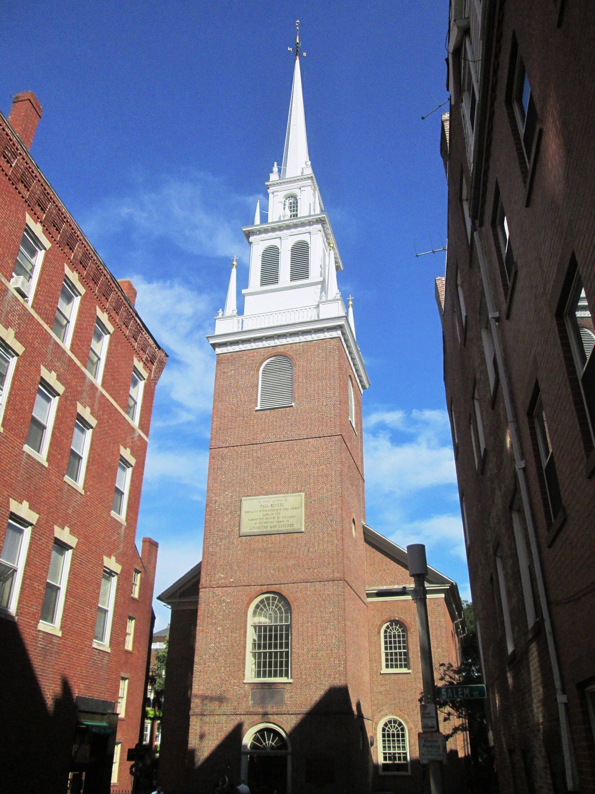 La façade en brique et le grand clocher blanc de l'Old North Church se dressent entre des bâtiments historiques en briques rouges sous un ciel bleu clair à Boston.