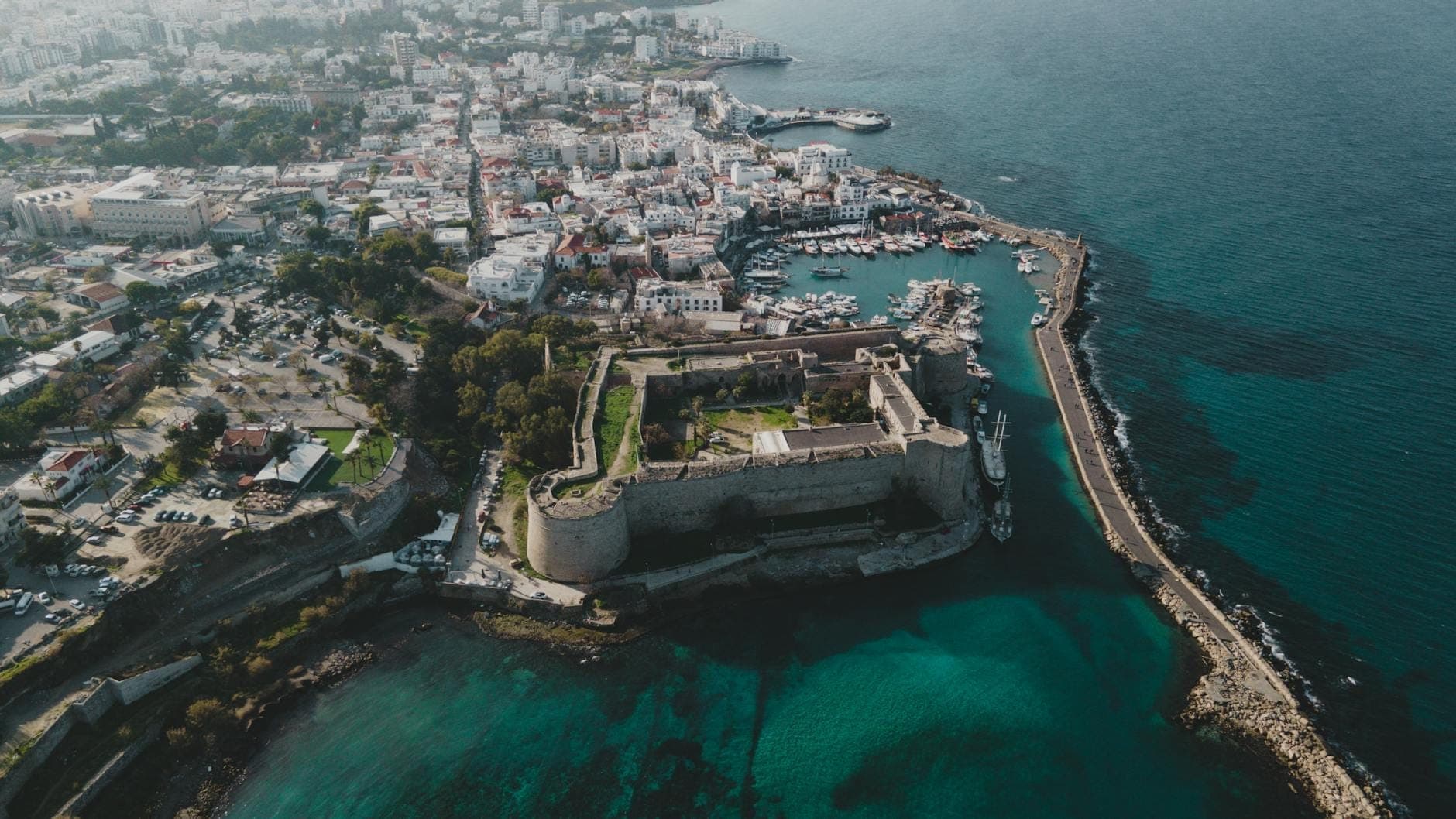 Vista aerea del porto di Rethymno con la grande fortezza veneziana circondata da acque turchesi, edifici della città e un lungo molo.