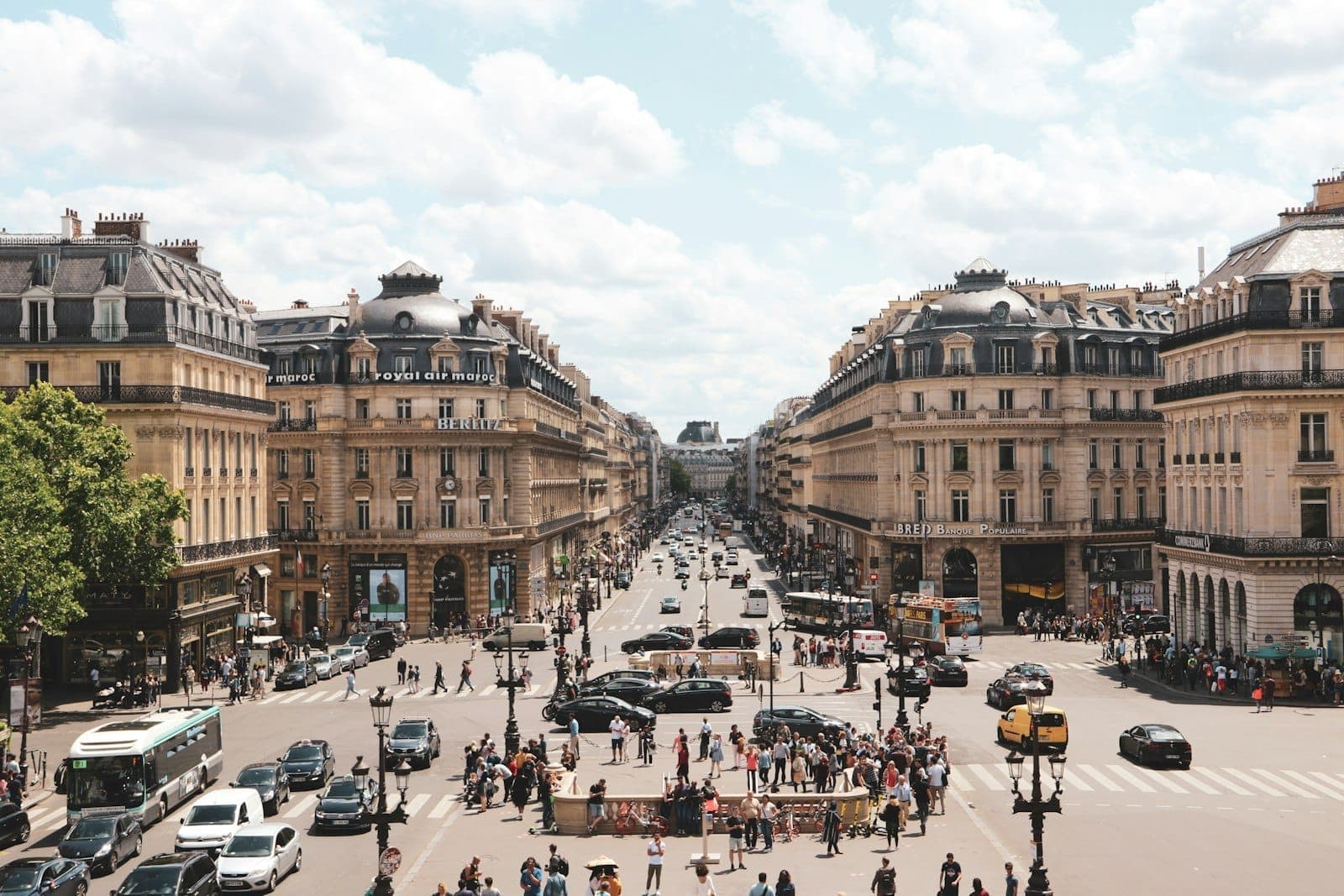 Wide view of Paris’s Grands Boulevards with classic Haussmann buildings, busy street scene, cars, and pedestrians under a partly cloudy sky.