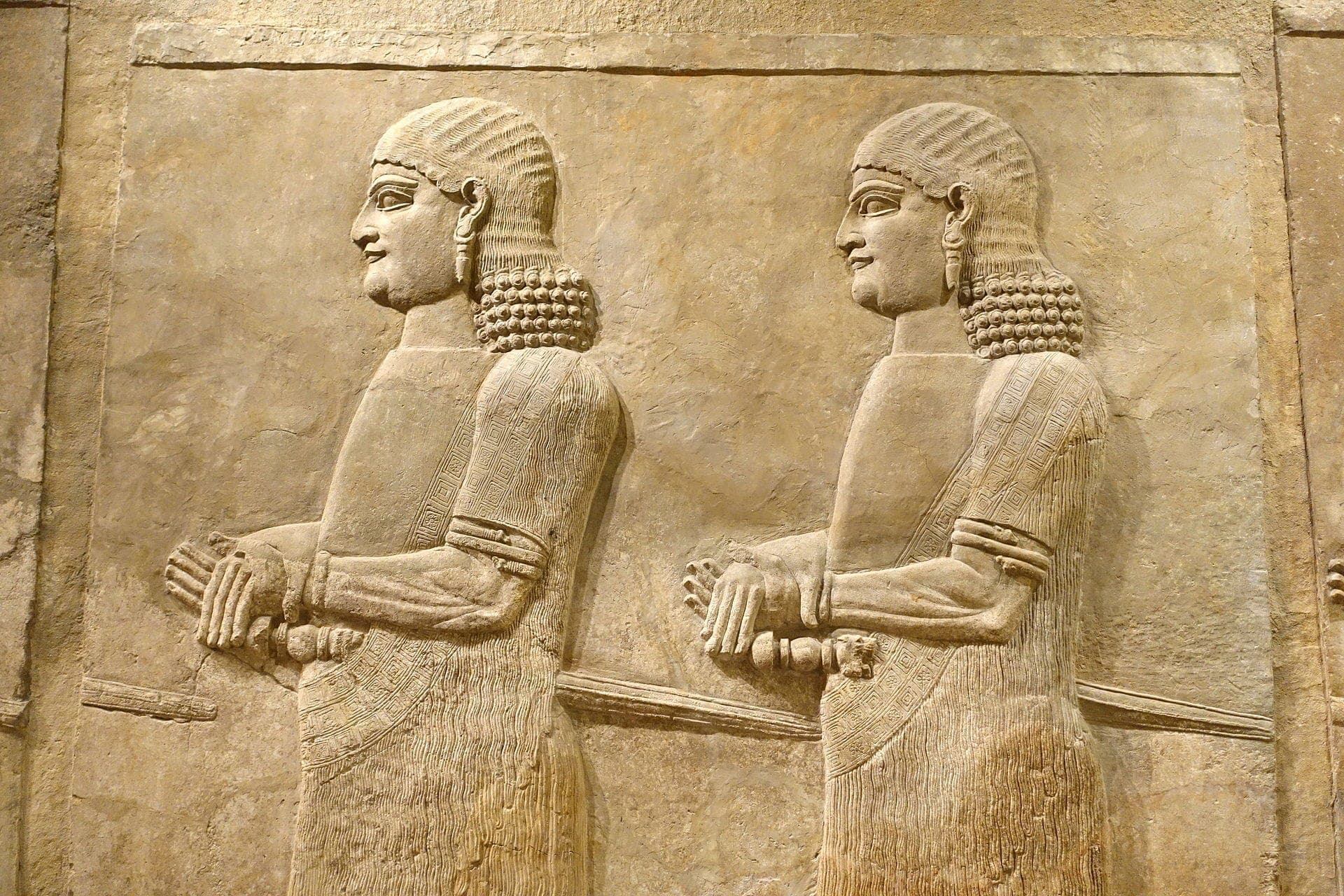 Relieve de piedra de dos figuras antiguas de perfil, con peinados y túnicas detallados, expuesto en el Institute for the Study of Ancient Cultures Museum.