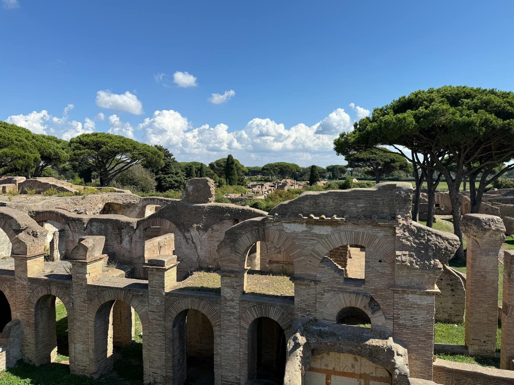 Panoramablick auf die Ruinen von Ostia Antica mit gewölbten Backsteinstrukturen und Schirmkiefern unter blauem Himmel.