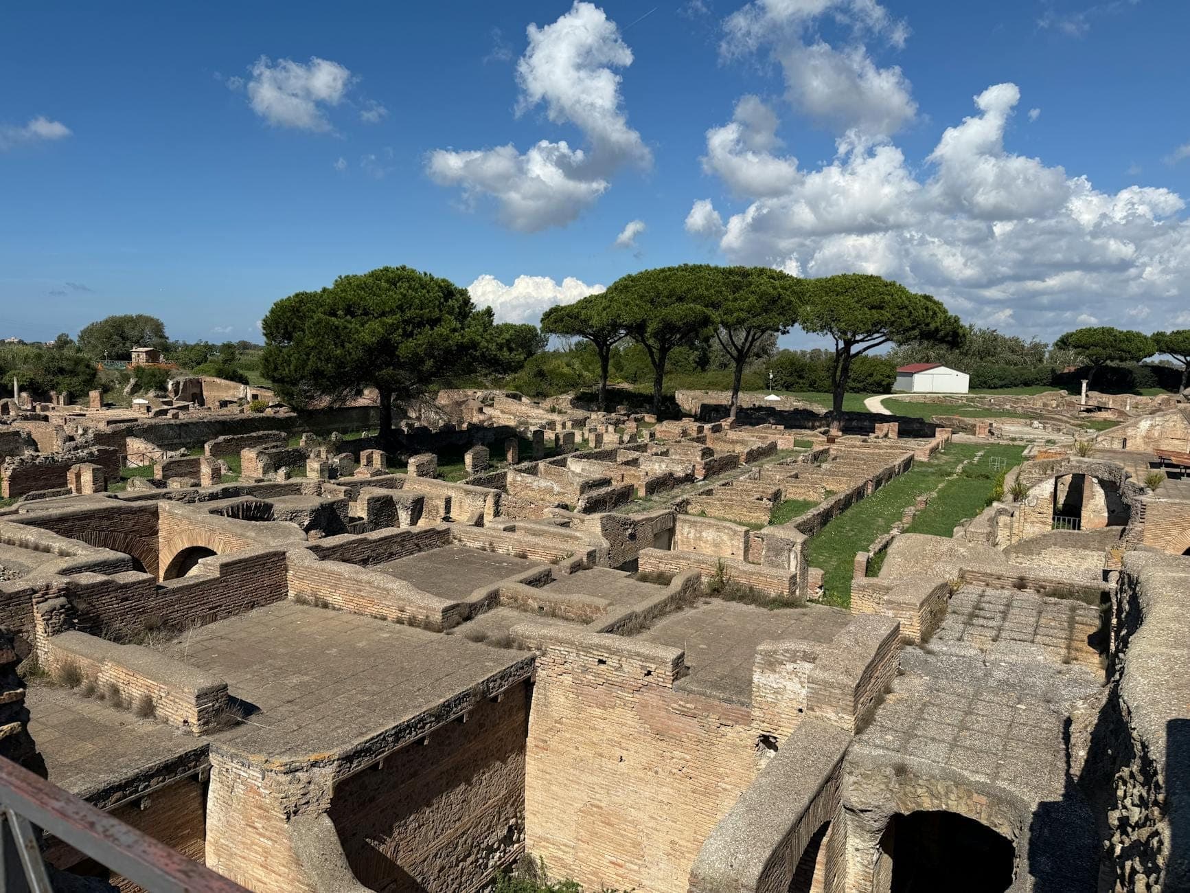 Weiter Blick auf die archäologischen Ruinen von Ostia Antica mit antiken Backsteingebäuden und Pinien unter einem sonnigen blauen Himmel.